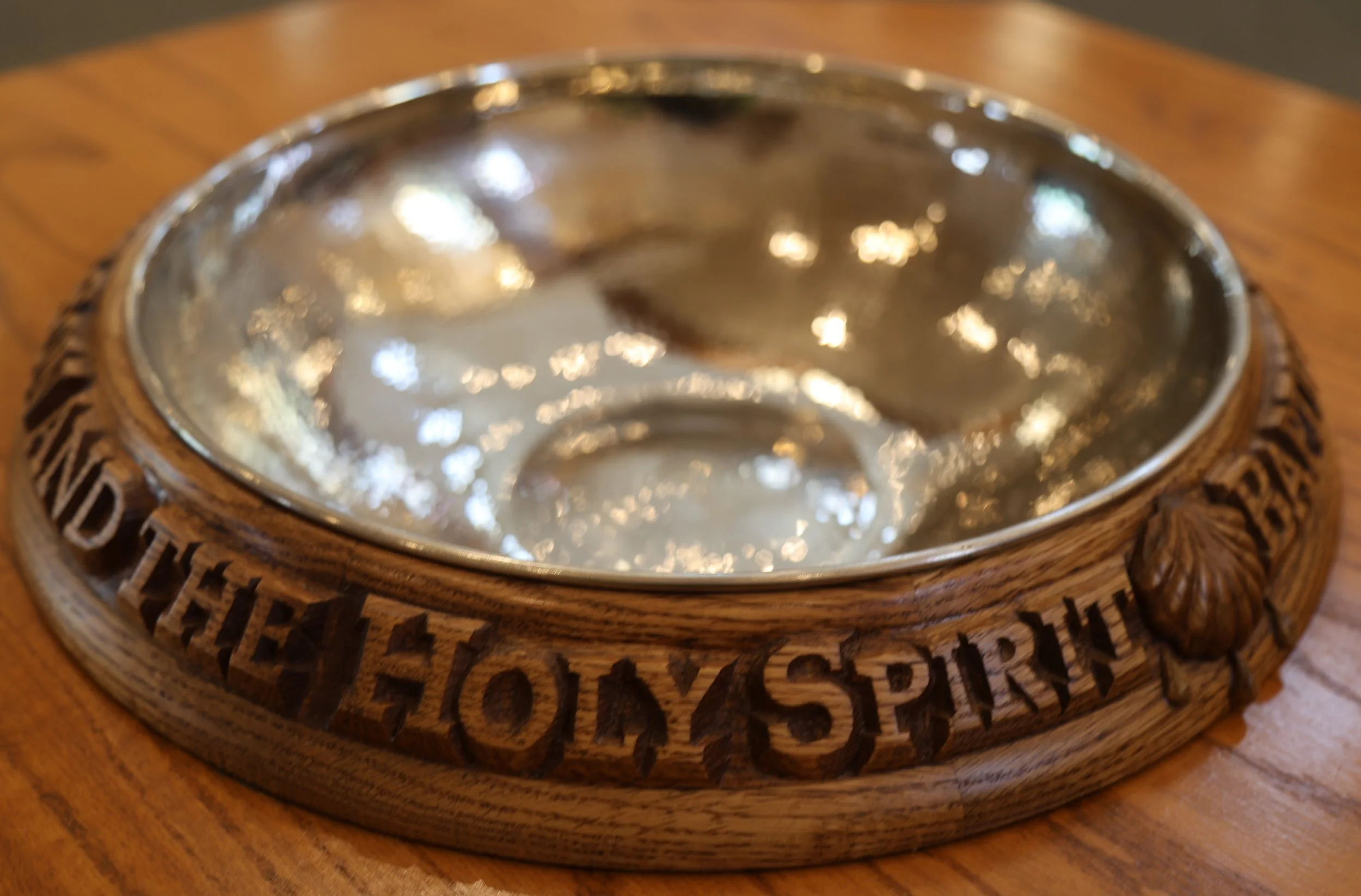 Our baptismal font has a wooden border engraved with the words "IN THE NAME OF THE FATHER, AND OF THE SON, AND OF THE HOLY SPIRIT".