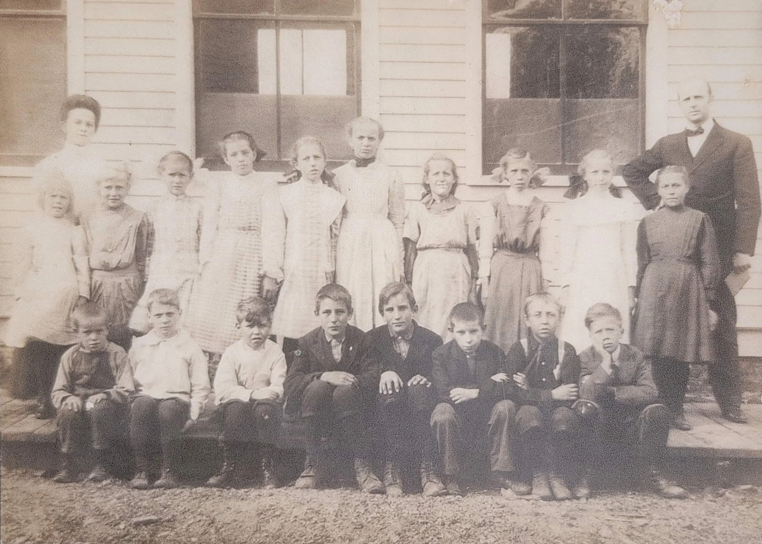 Historical photo of St. Paul's. Black and white photo of a group of children and two adults standing and sitting in front of a wooden building with two windows.