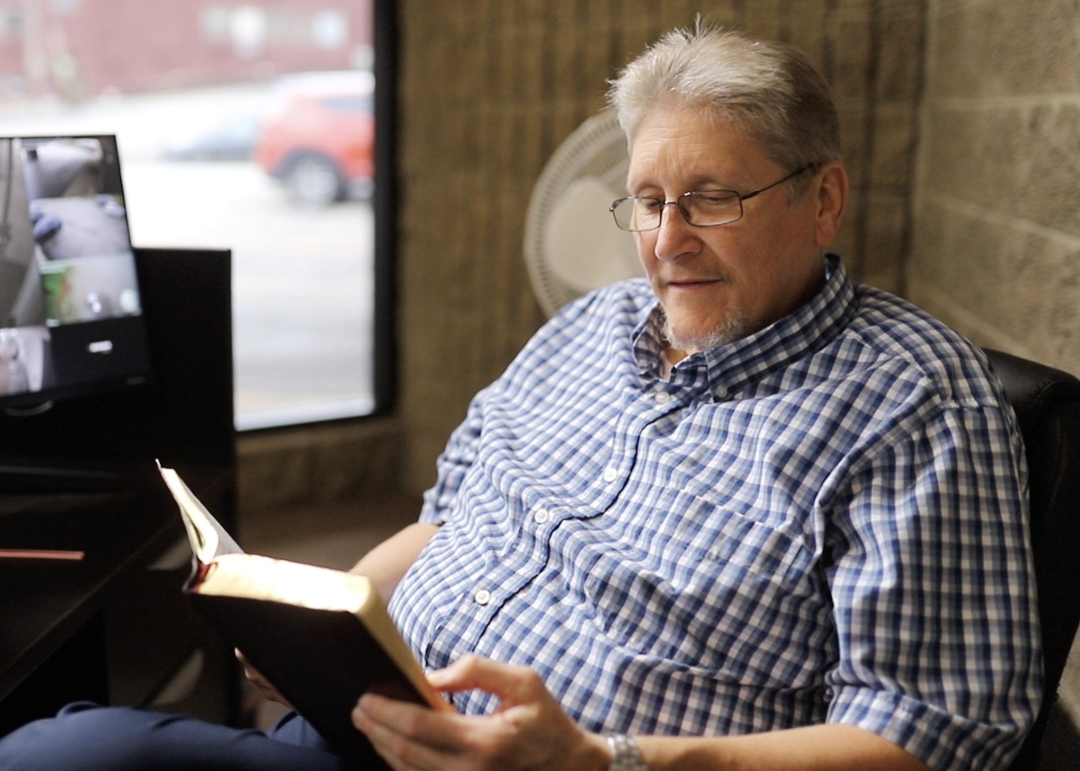 A man with glasses and gray hair reading a book while sitting in a cozy coffee shop.