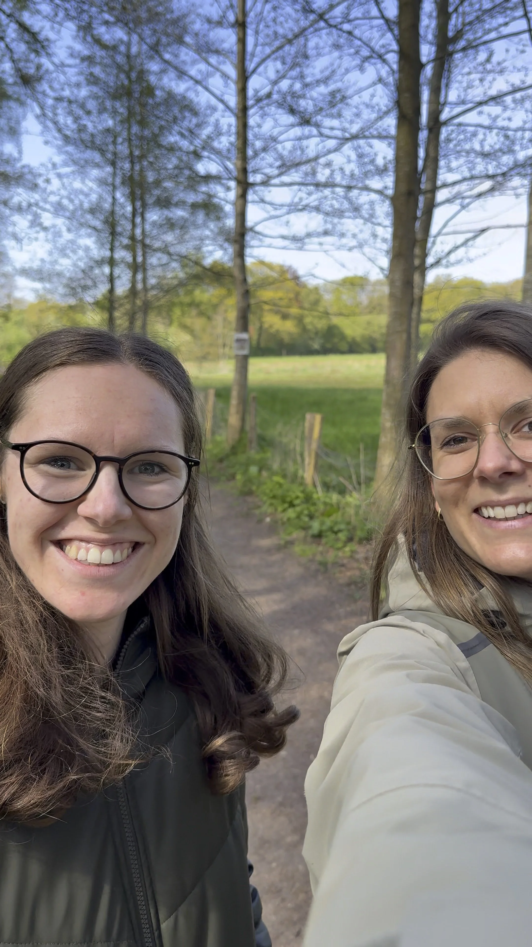 Zwei Frauen machen während eines Coaching Spaziergangs im Grünen ein Selfie.