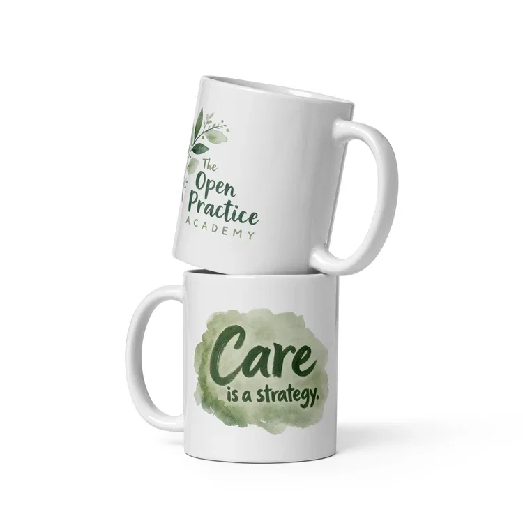 Two white coffee mugs stacked, one on top of the other. The top mug has a logo for 'The Open Practice Academy' with a green leaf design. The bottom mug has a green watercolor background with the text 'Care is a strategy.'