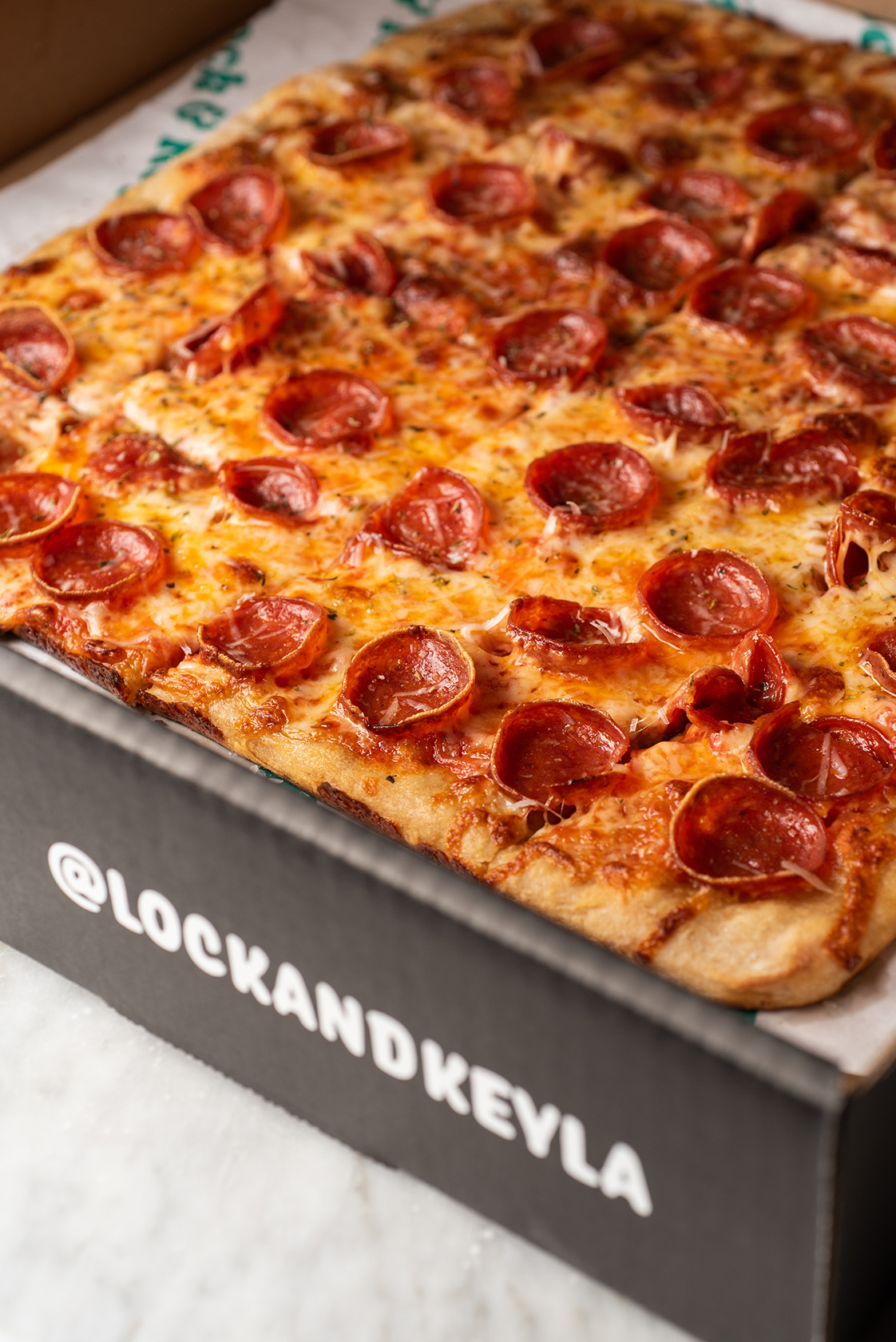 A pepperoni pizza in a black pizza box with '@LOCKANDKEYLA' printed on the side