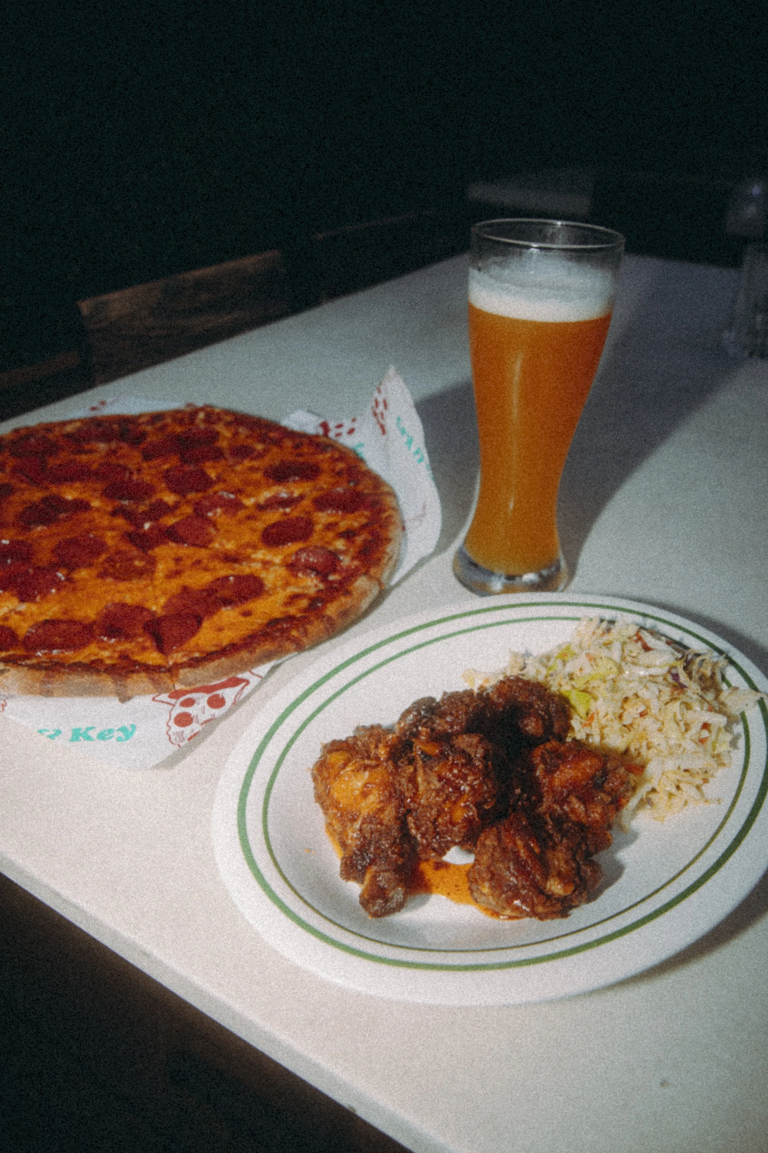 Pizza, fish with coleslaw, and a glass of beer on a white table.