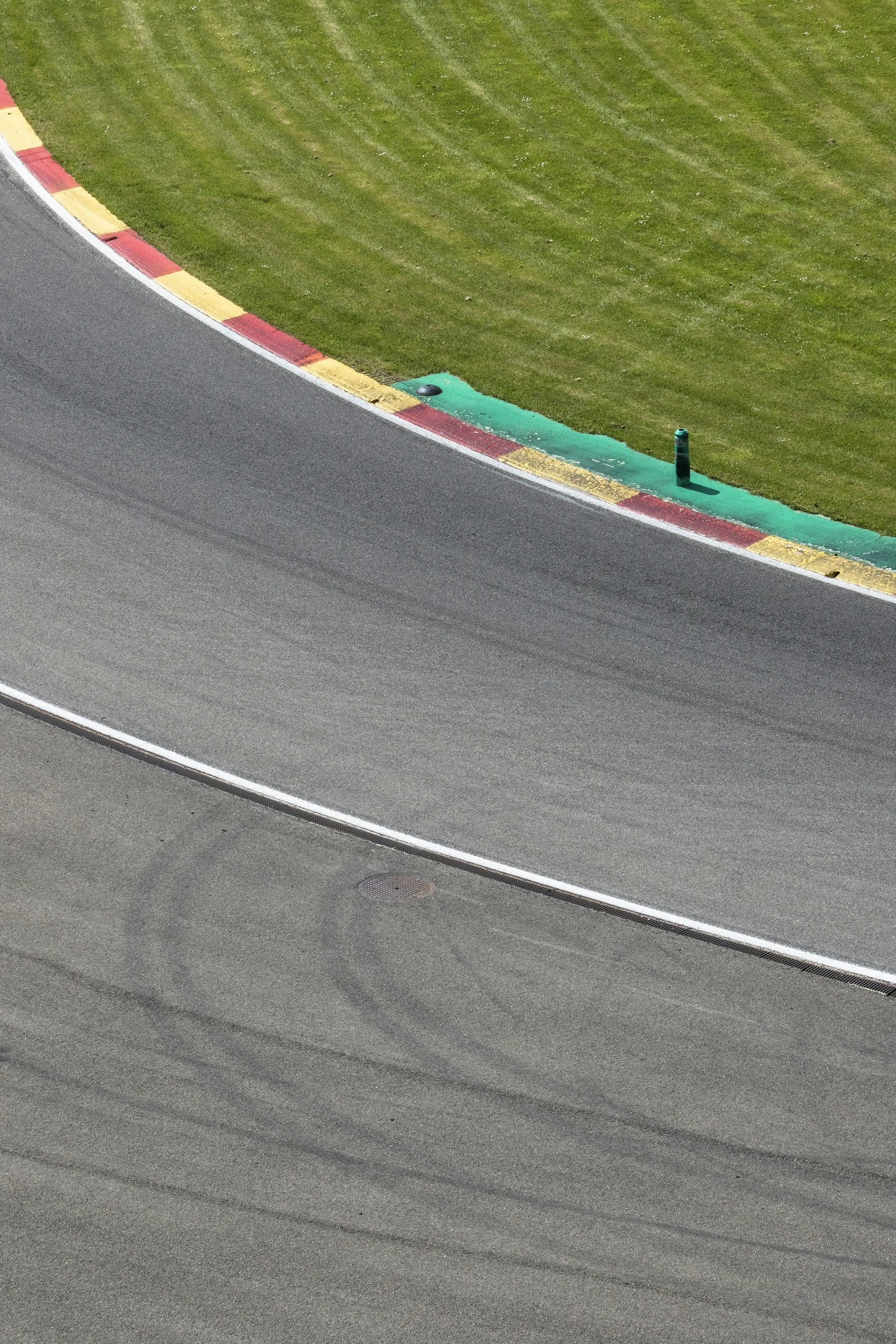 Close-up of a racetrack corner with a curb painted in red and yellow, surrounded by green grass.