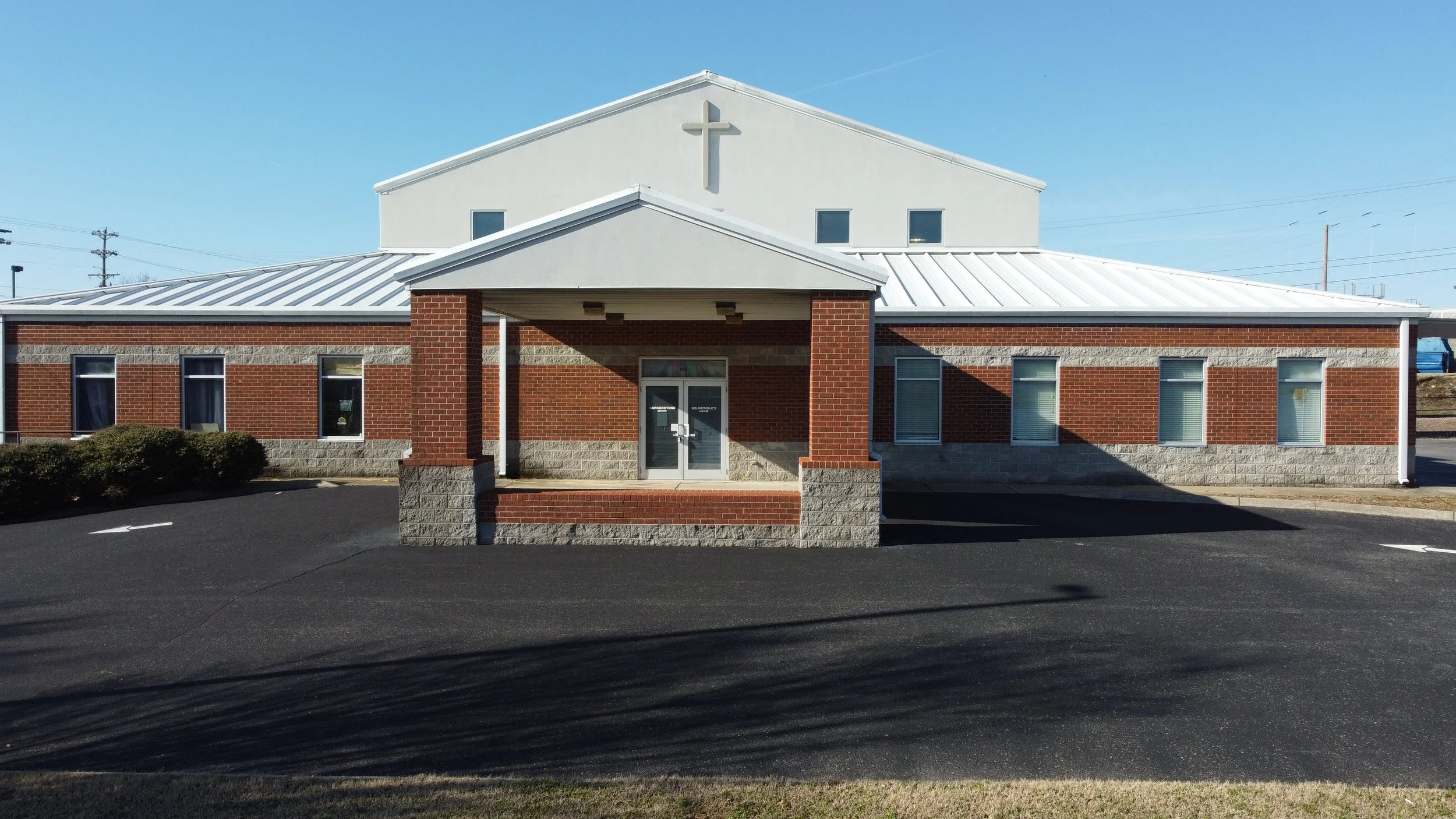 Exterior image of MNI Kids in Smyrna, TN with a brick lower section and a covered entrance with glass doors, located on a paved parking lot under a clear blue sky.