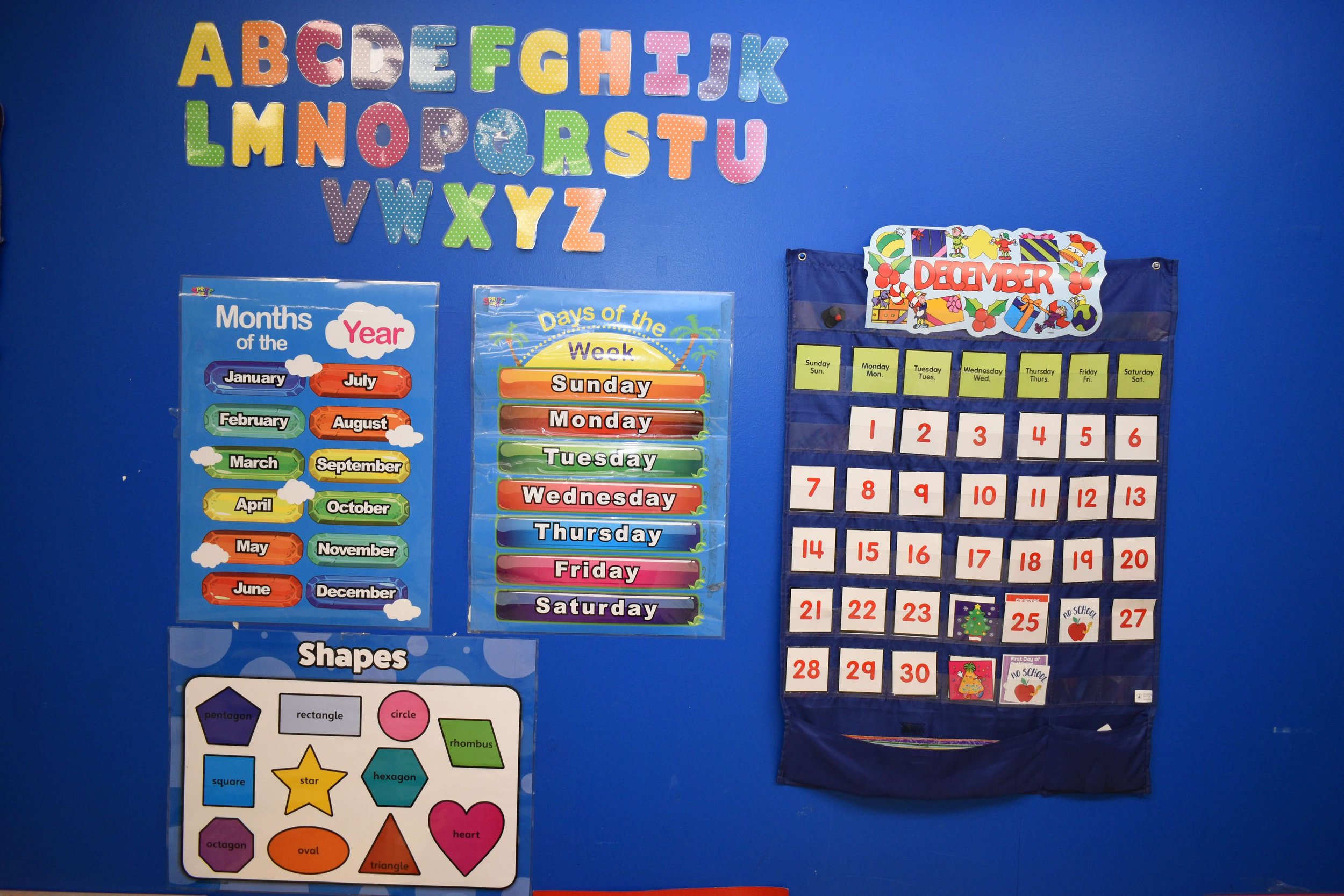 Colorful educational classroom wall with alphabet letters, months, days of the week, December calendar, and shapes posters.
