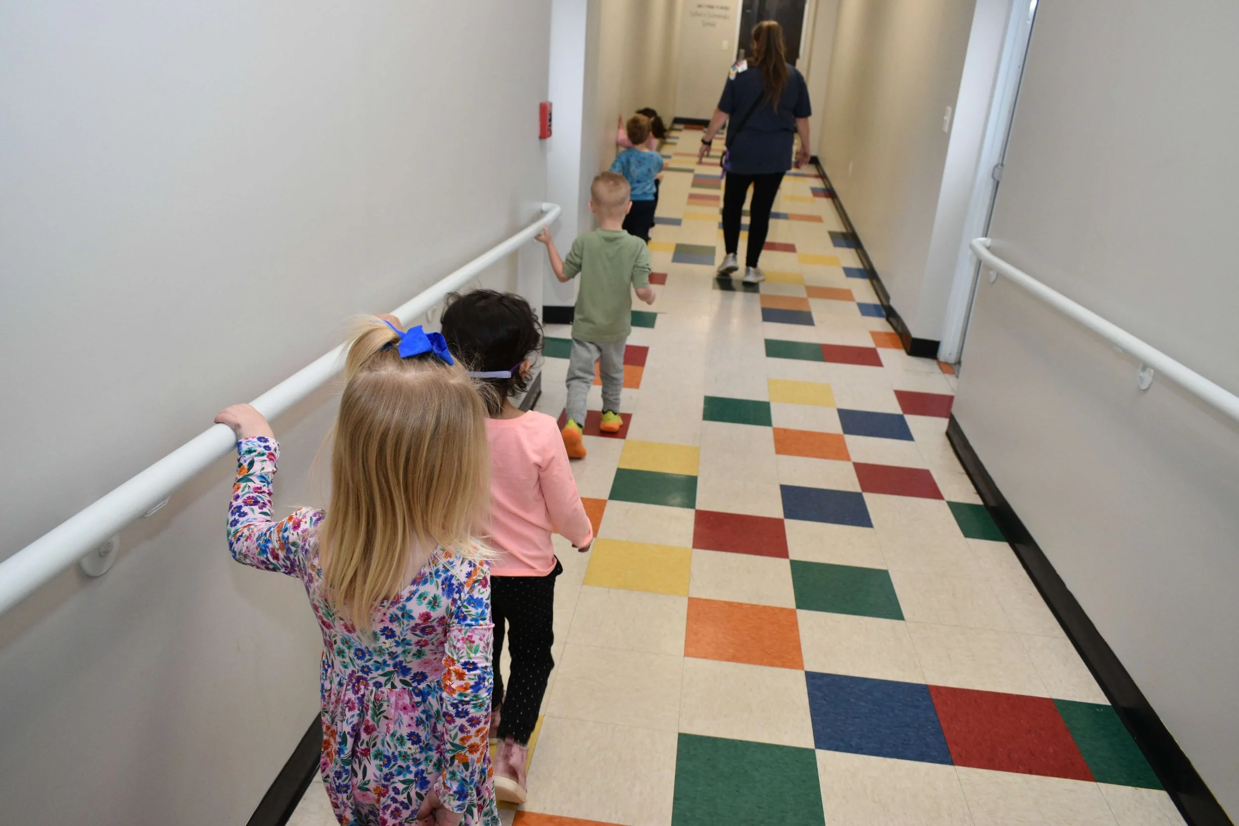 Children and a nurse walking down a colorful hospital hallway, practicing social distancing.