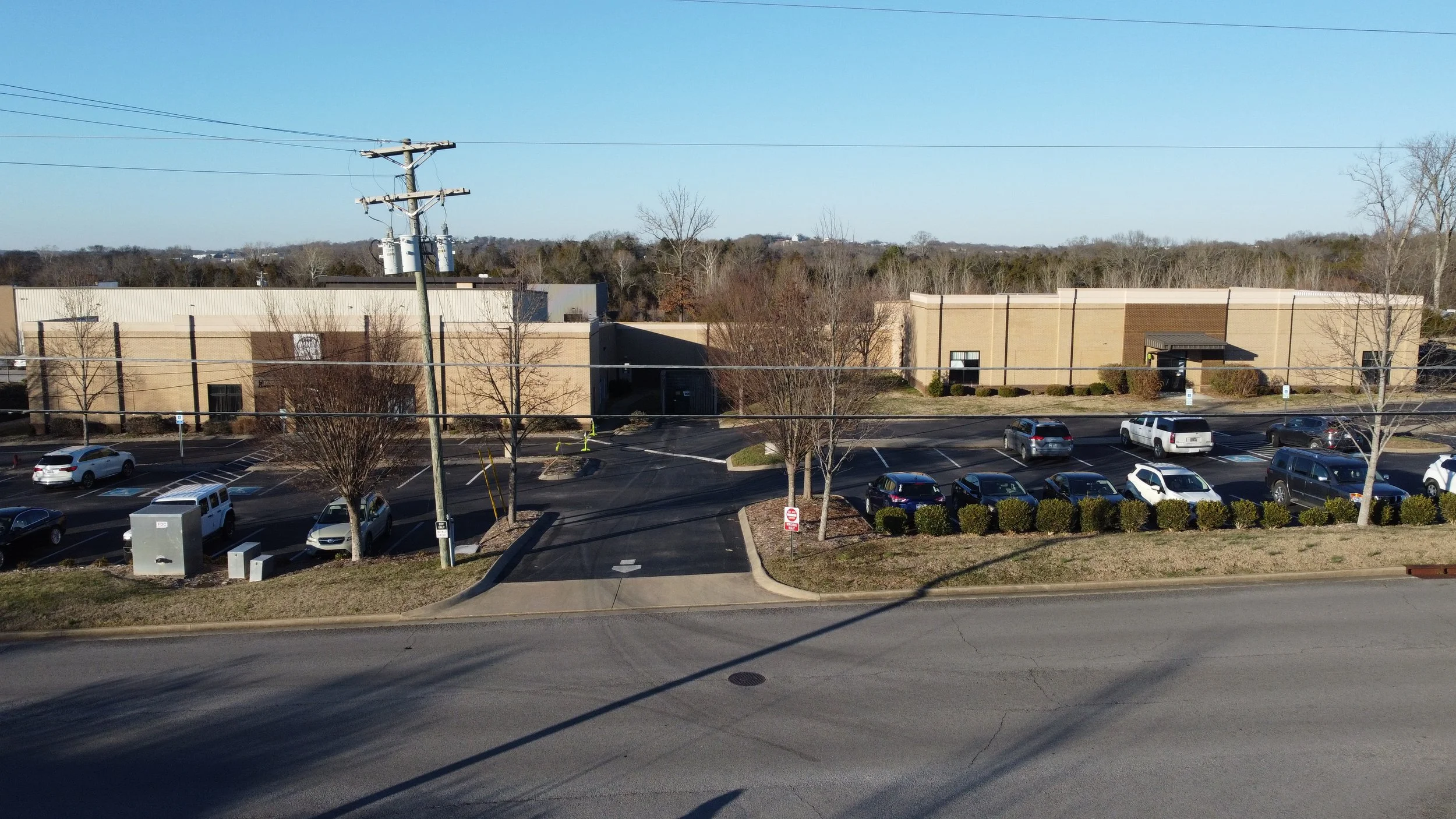 A parking lot outside MNI Kids Nolenville with several parked cars and leafless trees, under a clear blue sky.