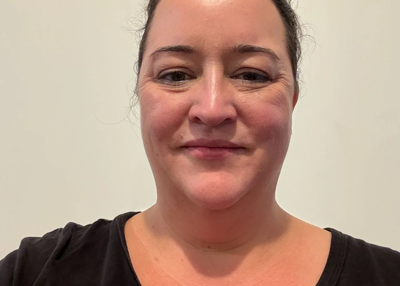 Close-up of a woman smiling, wearing a black top, against a plain light background.