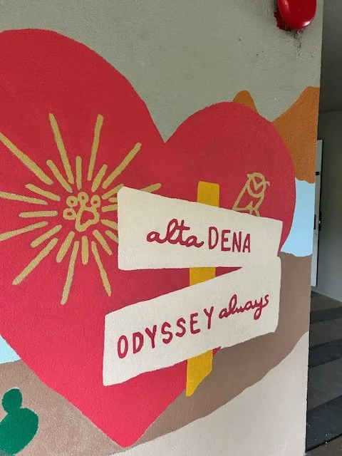 Colorful mural featuring a large red heart with yellow decorative lines, a sign reading 'alta DENA' and 'ODYSSEY always', and other artistic elements.
