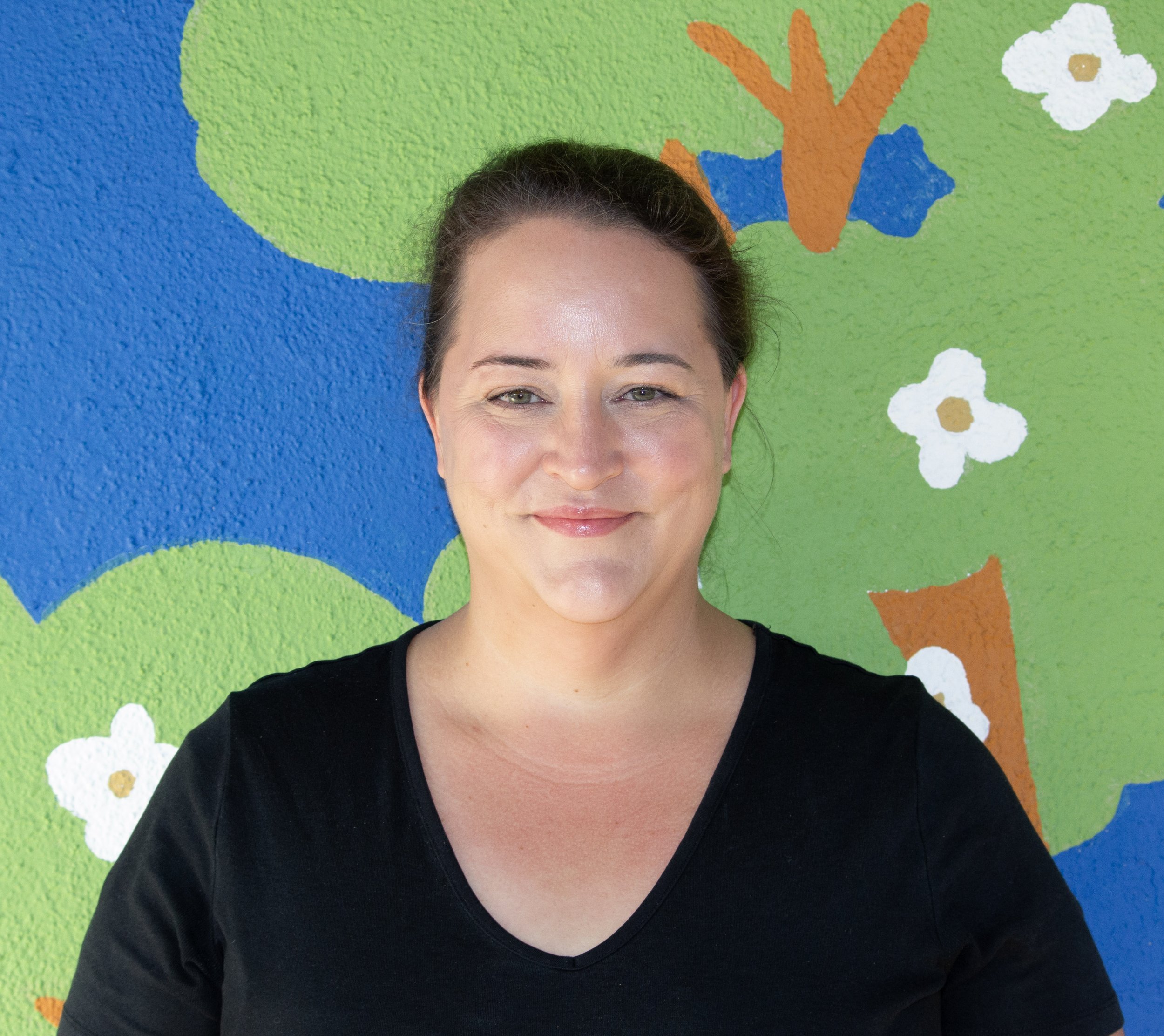 Close-up of a woman smiling, wearing a black top, against a plain light background.