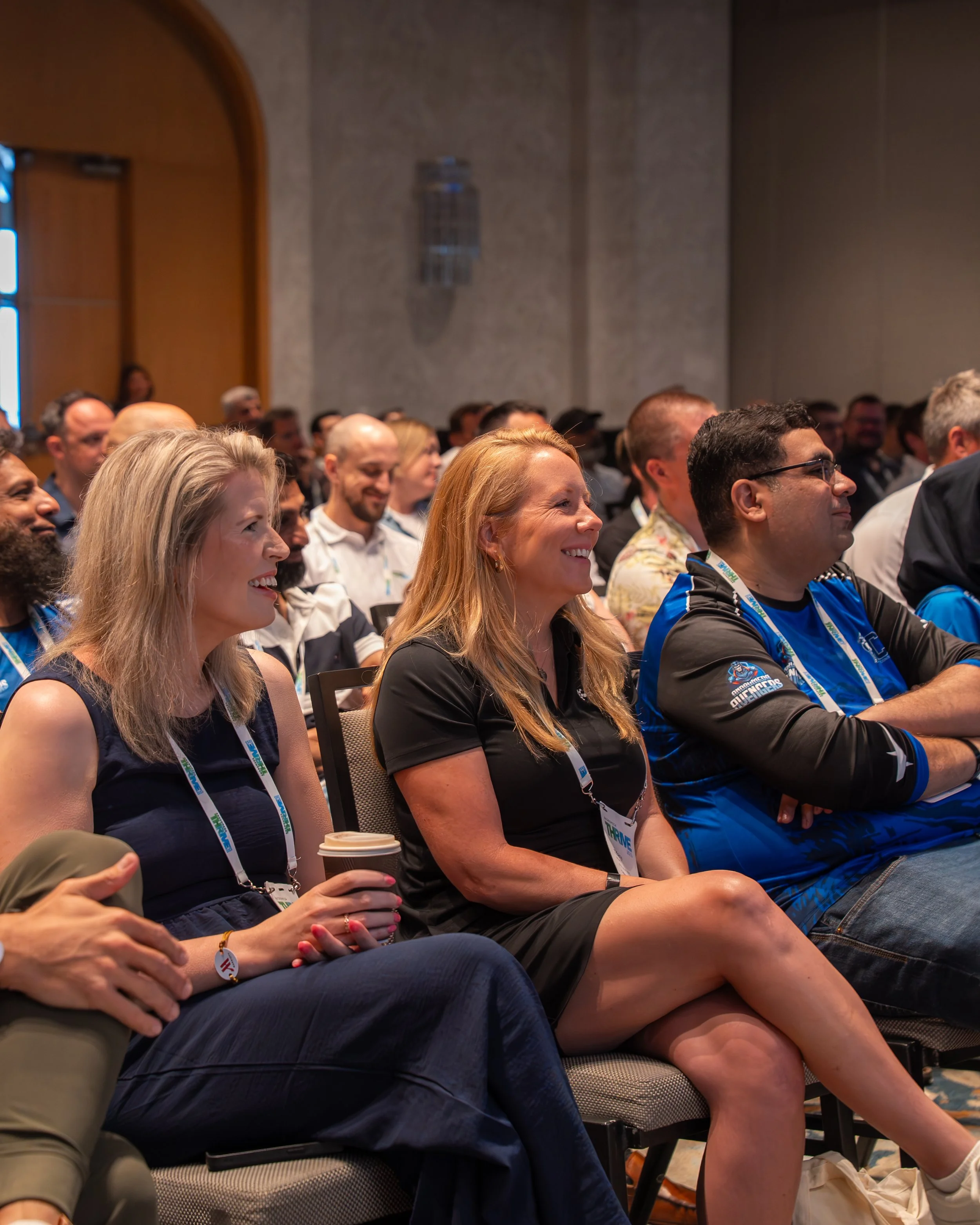 Audience attending a conference, sitting in chairs, smiling, and enjoying the presentation.