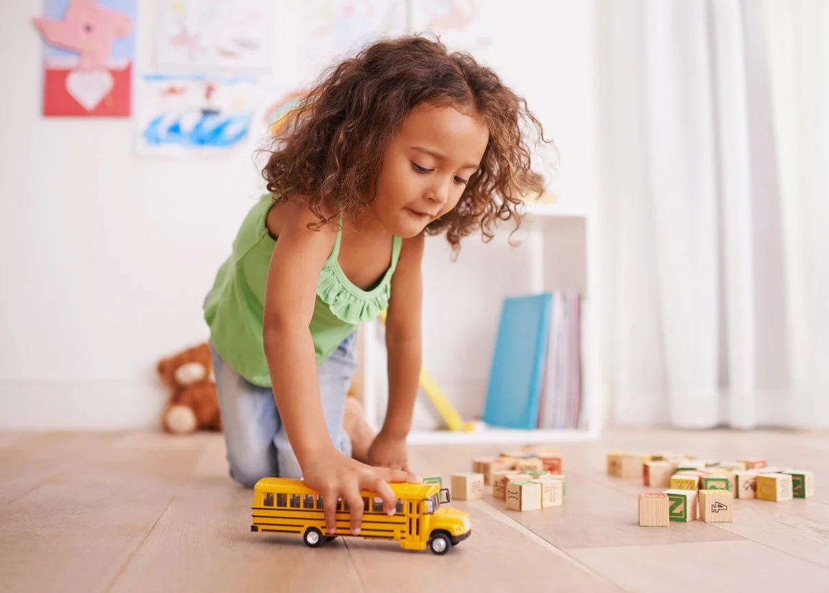 A young girl playing with a yellow toy school bus on the floor during play-based speech therapy in Las Vegas, NV