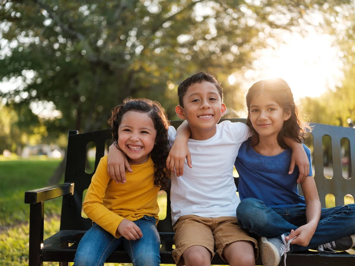 Three children sitting on a bench, smiling, with improved communication because of speech therapy for kids in Las Vegas, NV