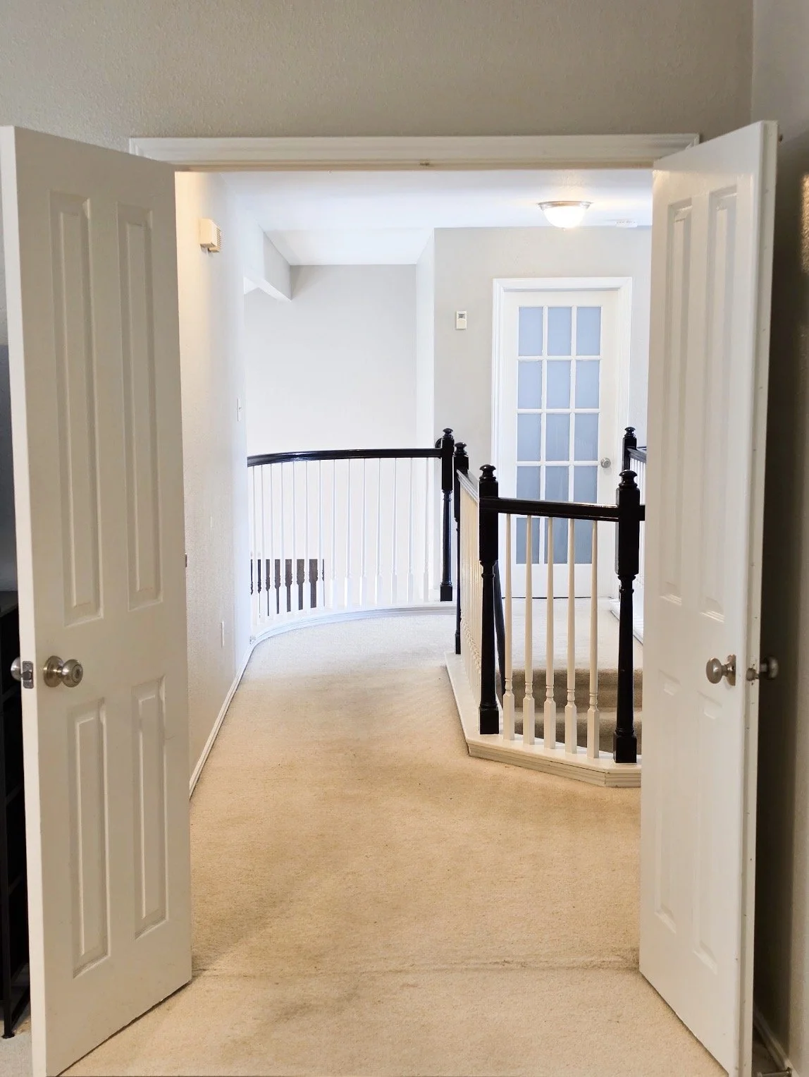 View from inside the large master bedroom on the second floor, showing another bedroom in the distance, hallway, and stairs at Fireside Sober Living.