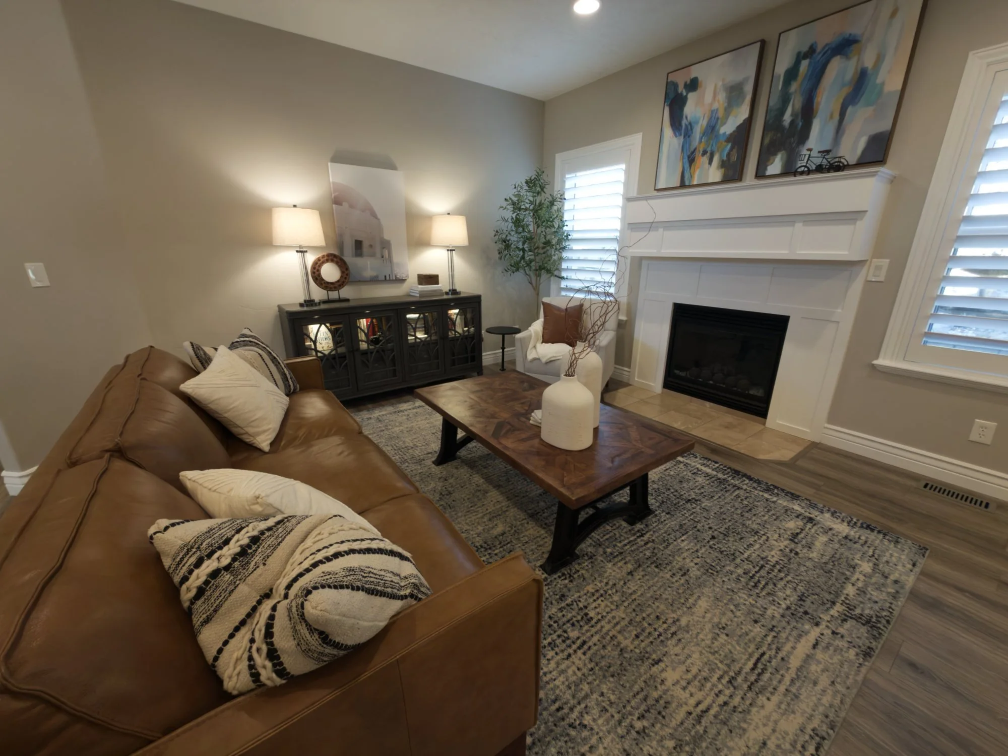 A custom decorated living room in Bountiful, UT with a brown leather sofa, a wooden coffee table with large white vases and a plush white armchair. Reclamation Home offers affordable custom decorating  and design services in Davis County. 