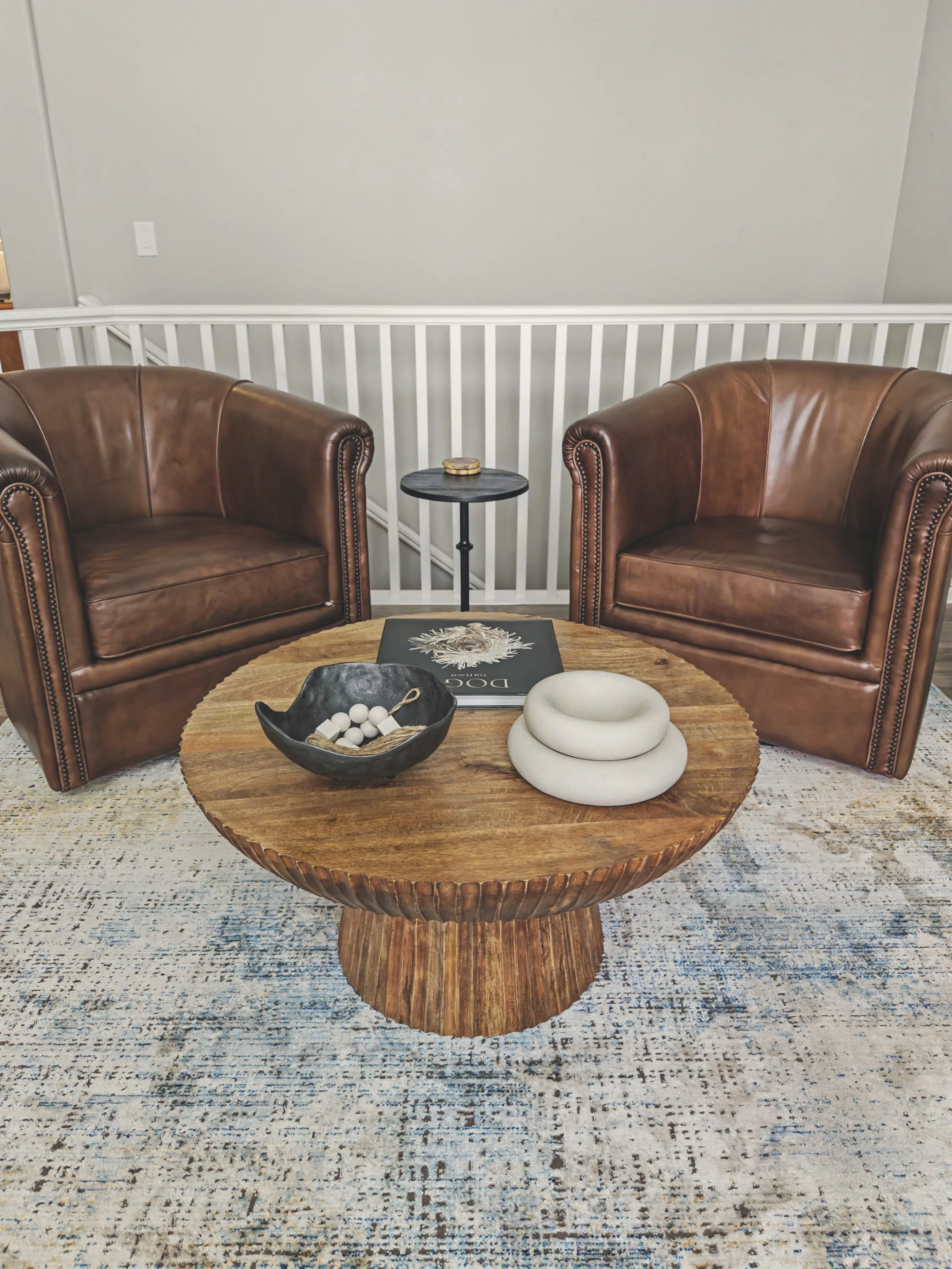 Living room with two brown leather armchairs, a wooden coffee table with decorative objects, a small round side table, and a patterned area rug. This room was decorated by Brock Abel, an interior designer in Davis County.