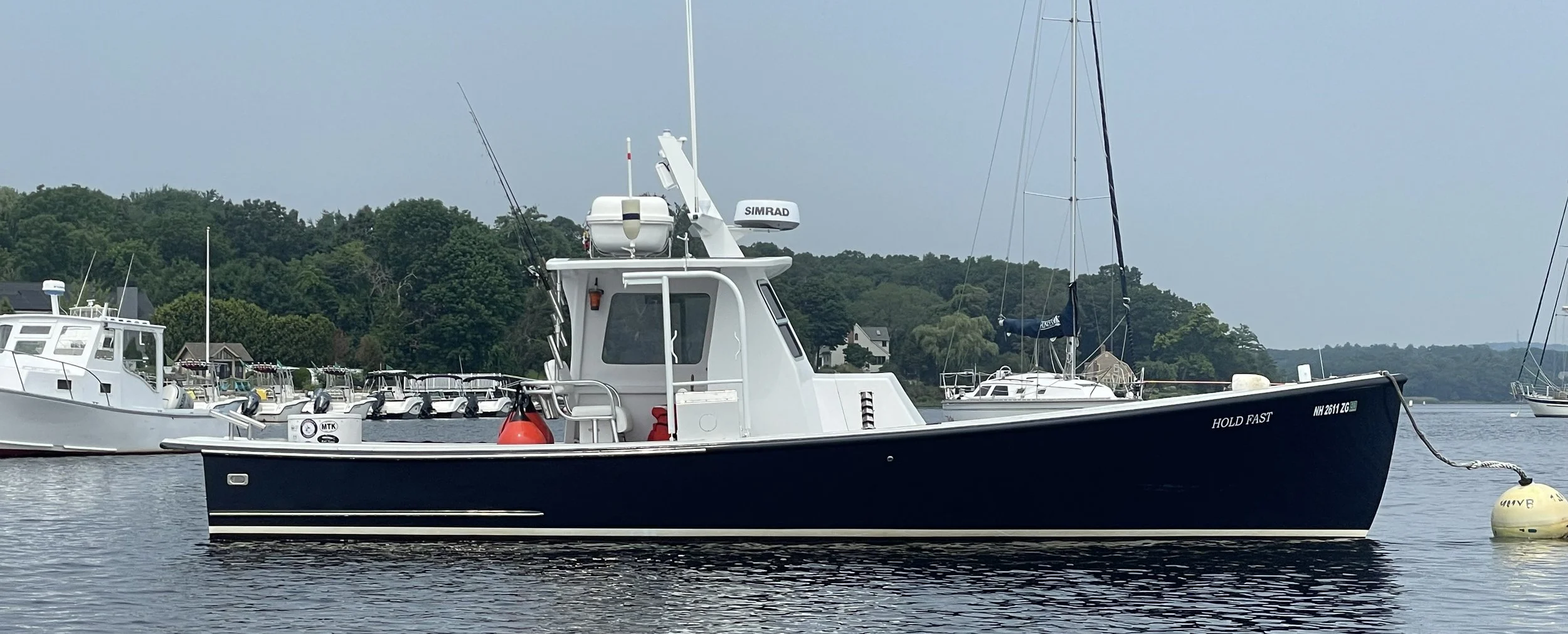 A boat named 'HOLD FAST' floating on water with other boats and green trees in the background.