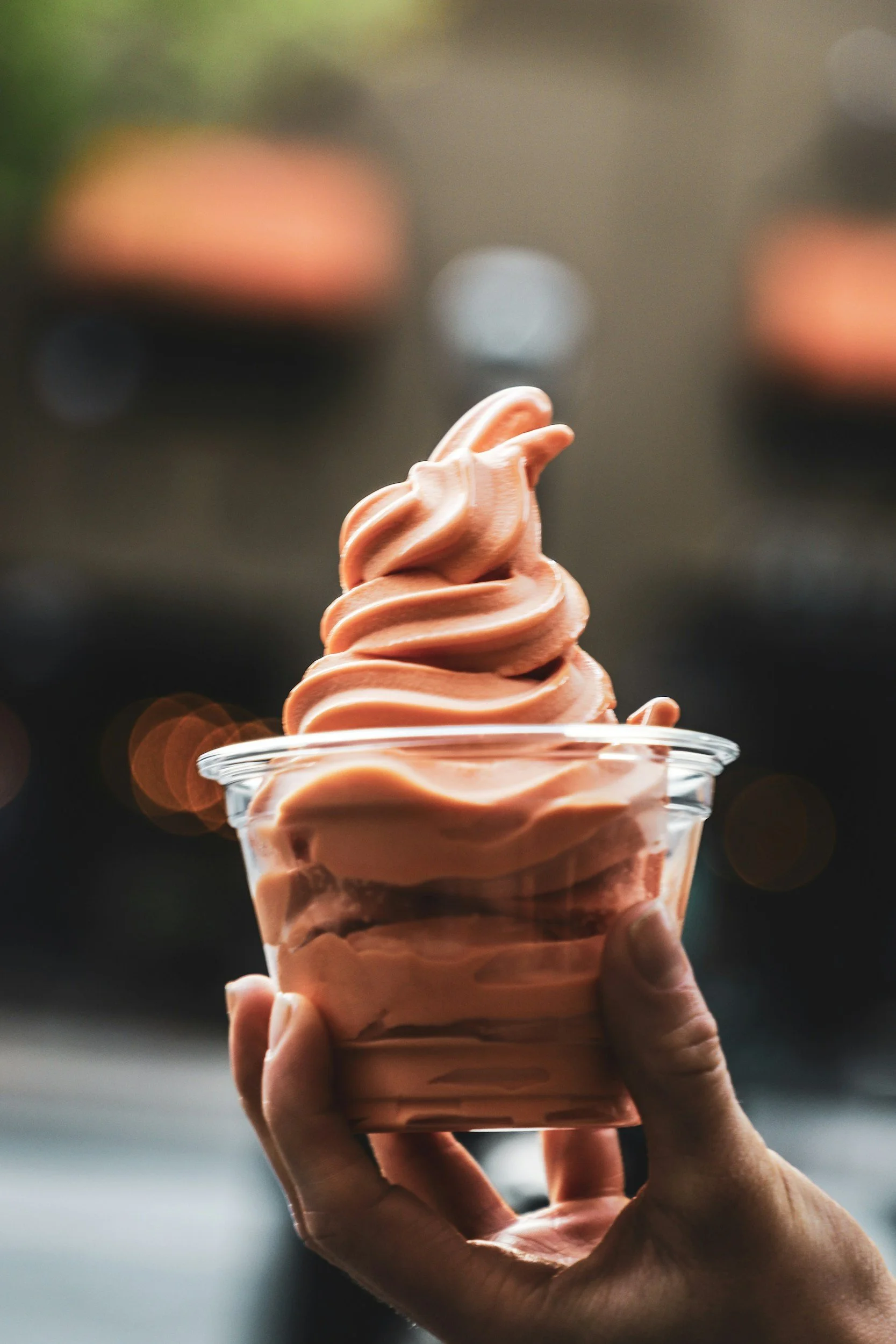 A hand holding a clear cup filled with swirled, pink soft serve ice cream.