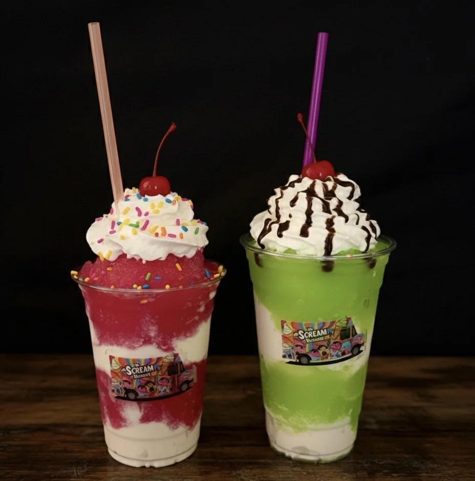 Two colorful milkshake drinks topped with whipped cream, cherries, and sprinkles in clear cups on a wooden surface against a black background.