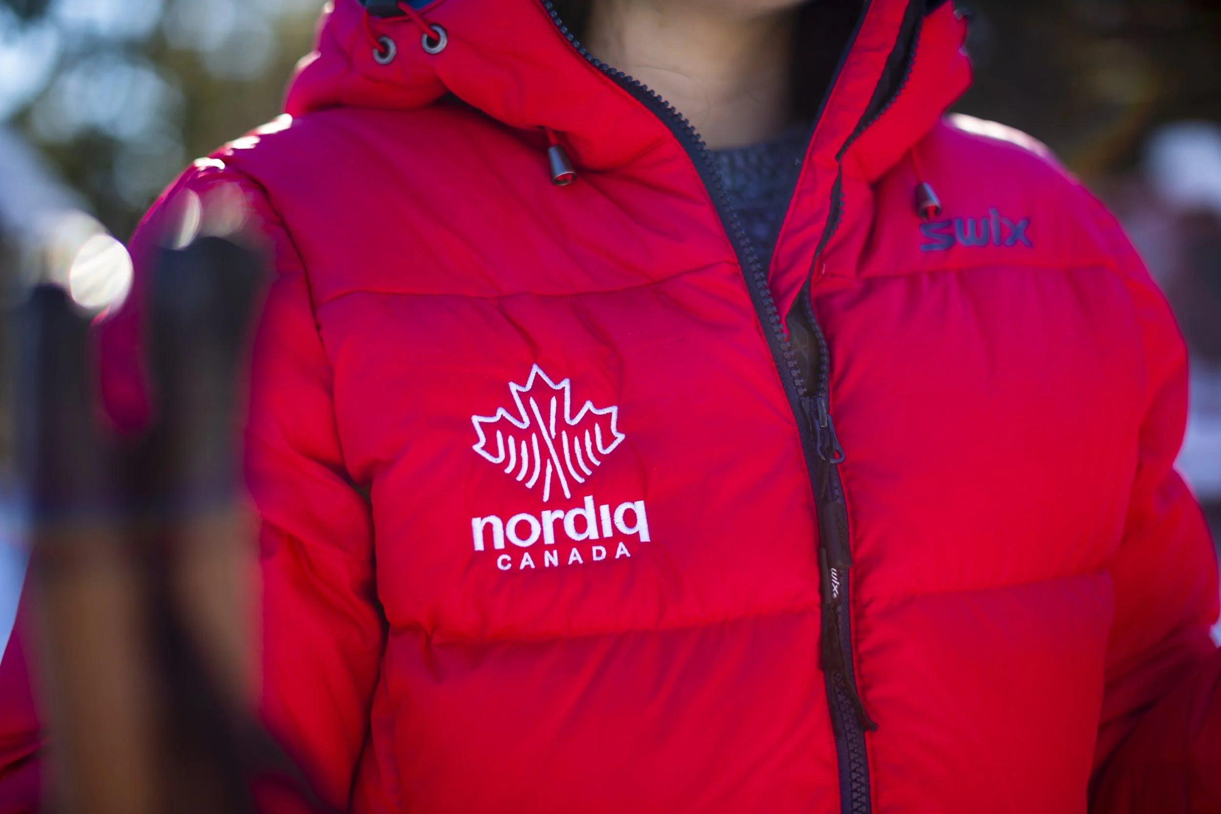 Close-up of a person wearing a red winter jacket with logos for Nordiq Canada and Swix, outdoors in a cold environment.
