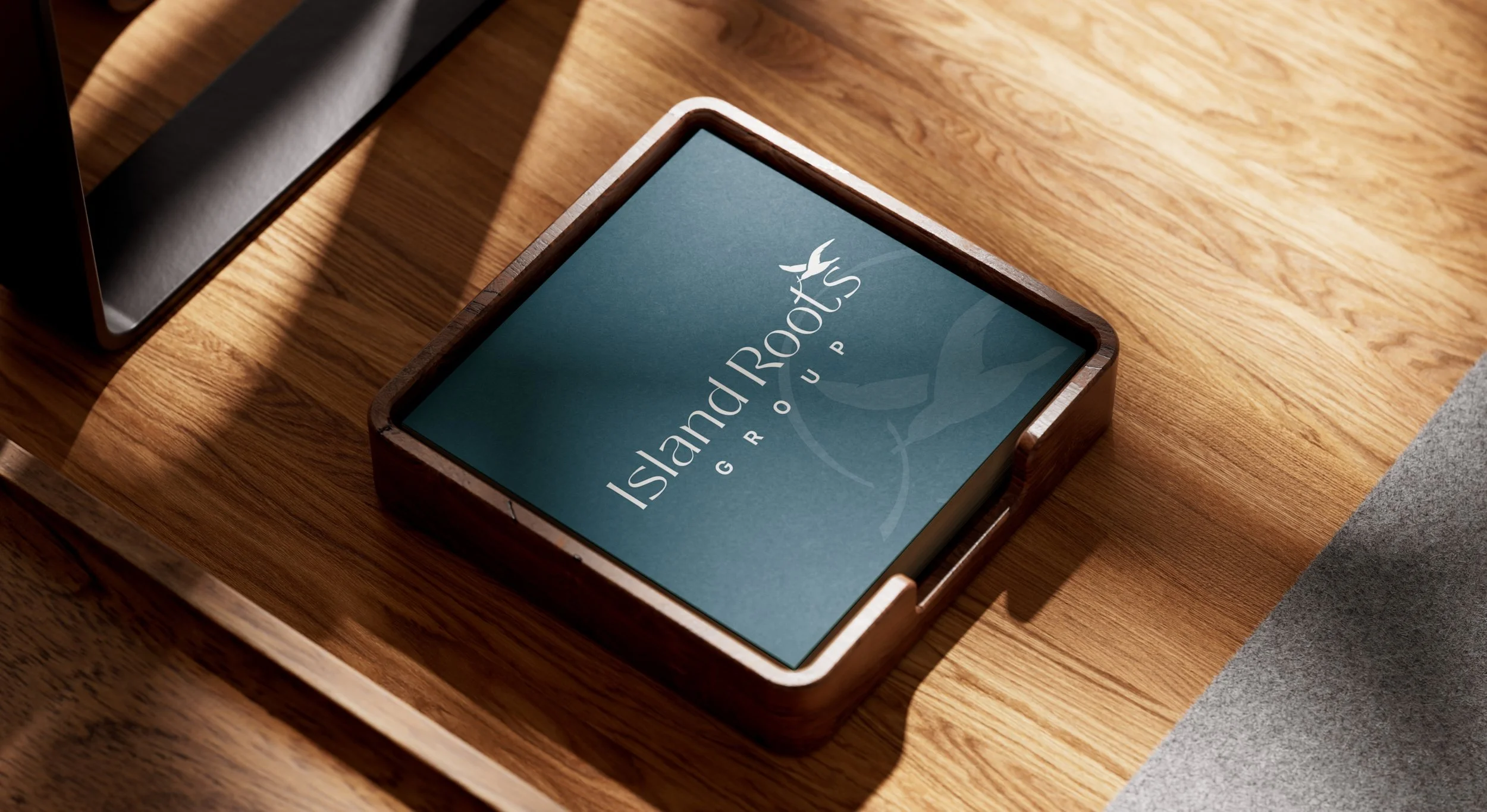 Wooden table with a tablet displaying the Islander Roots Group logo, and a laptop partially visible on the left side.