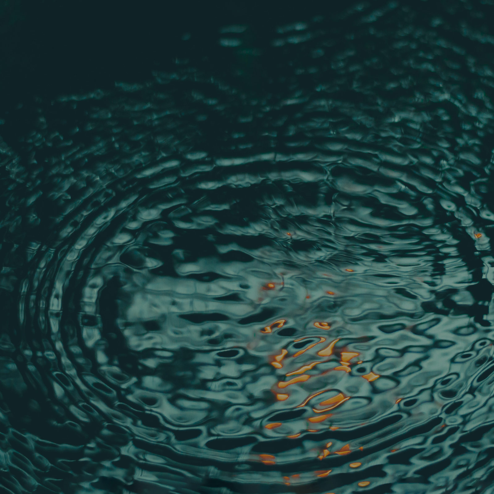 Close-up of water with ripples and reflections, with faint orange highlights.