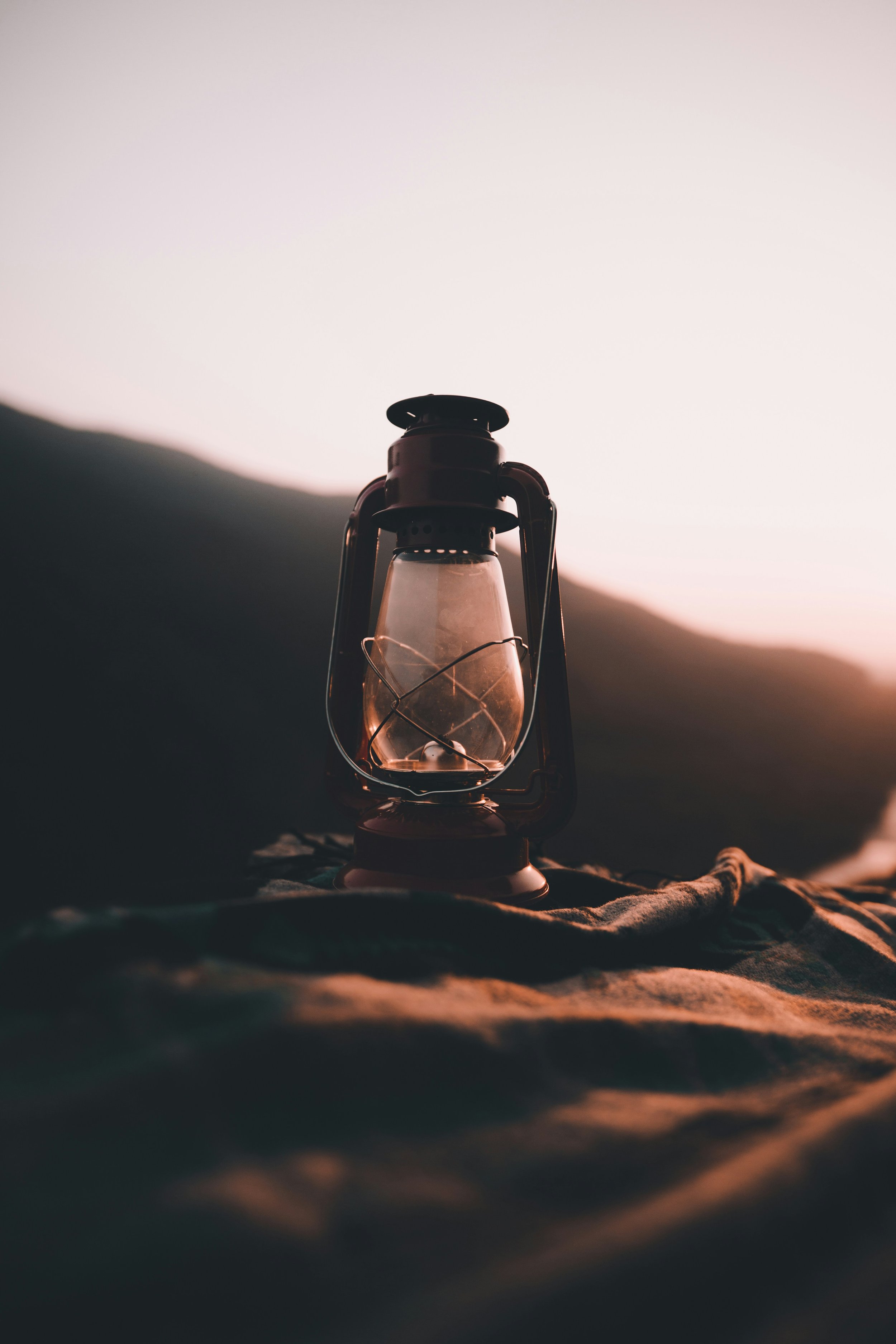 A vintage lantern on a blanket outdoors at sunset or sunrise.