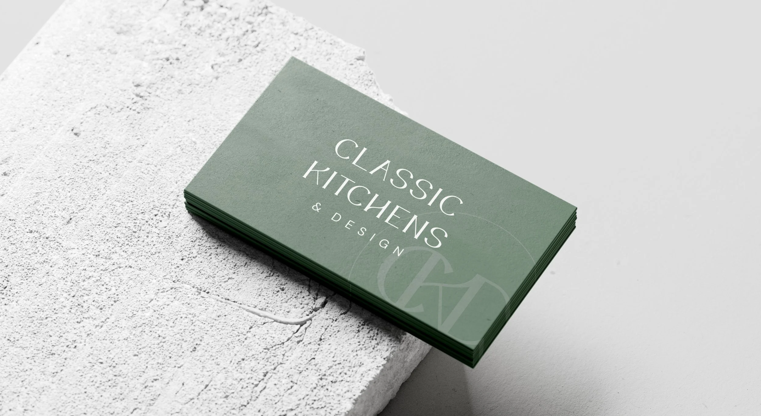 Stack of green business cards with white text reading 'Classic Kitchens & Design' placed on a white textured surface.