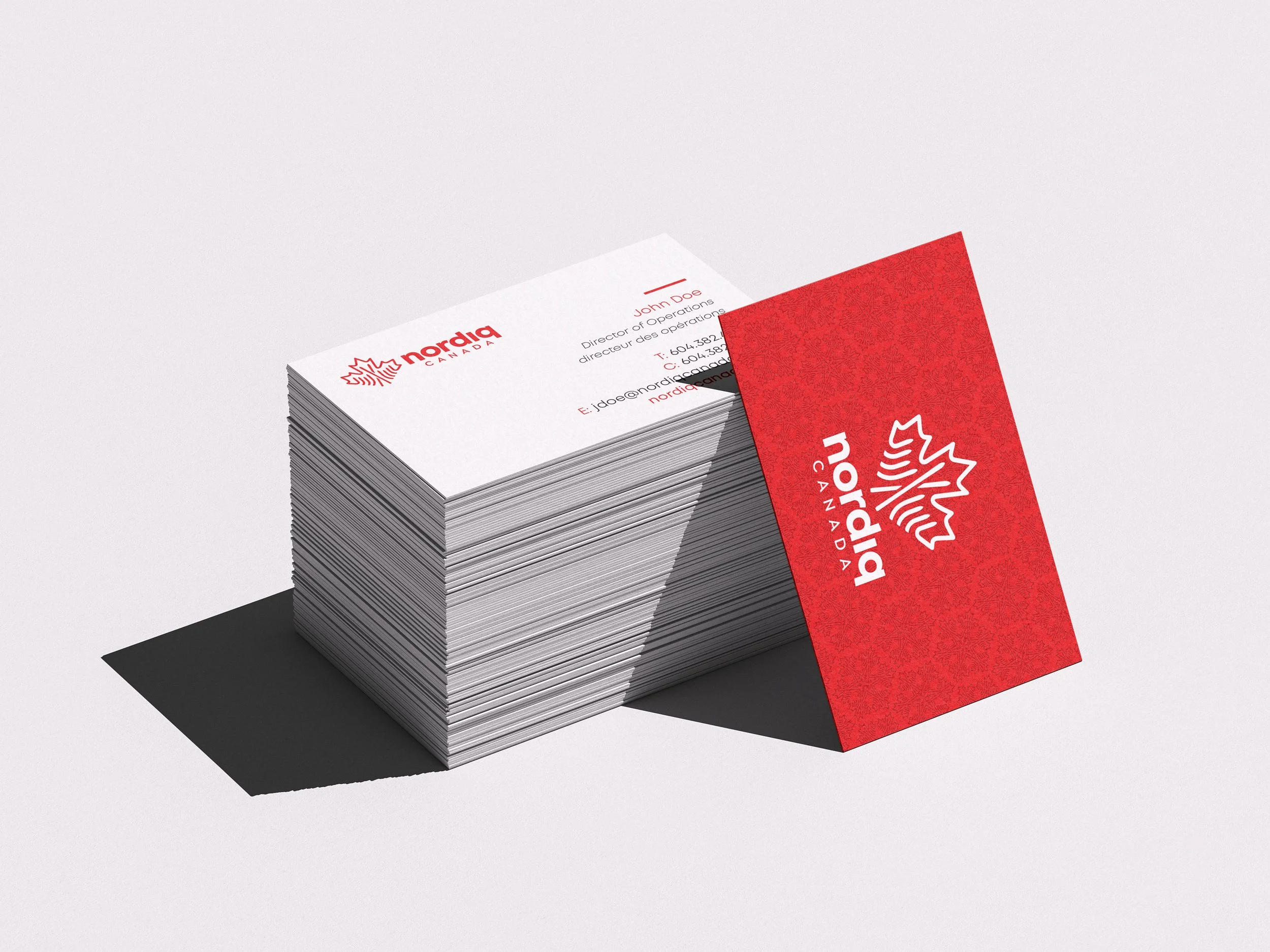 Stack of white business cards with red and black text and logo against a white background, with one card leaning upright showing the front design.