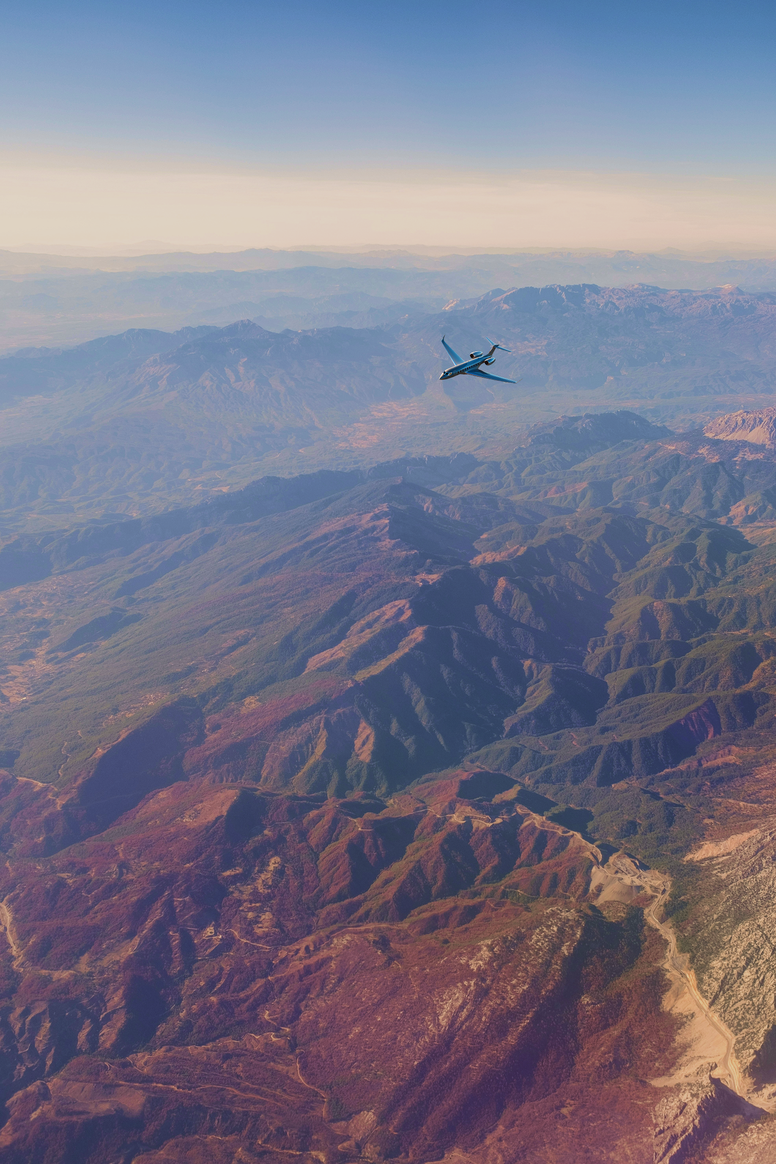 A plane flying over a mountainous landscape with a clear sky.