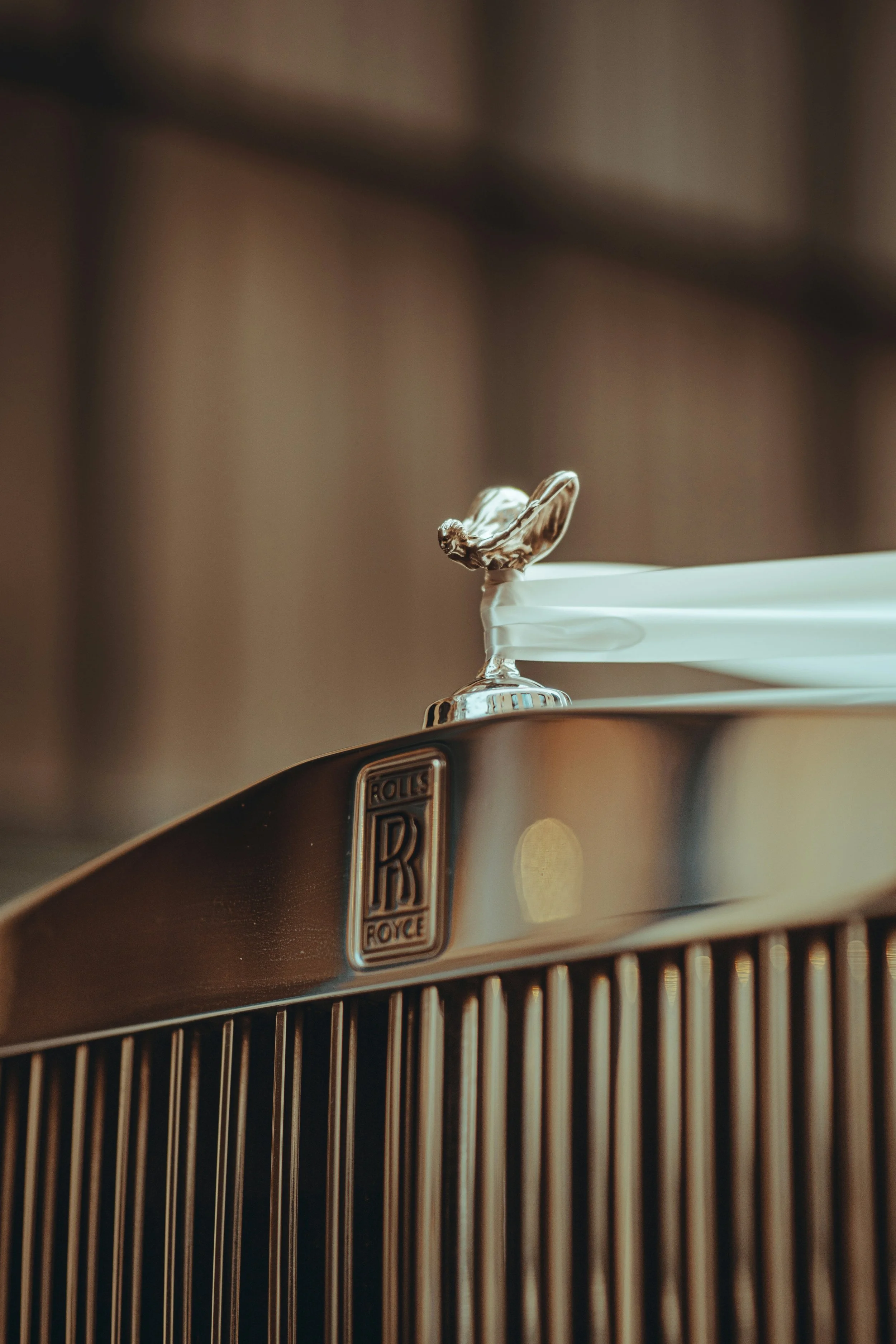 Close-up of a vintage Rolls Royces radiator grille with a silver Spirit of Ecstasy hood ornament and a tissue box on top.