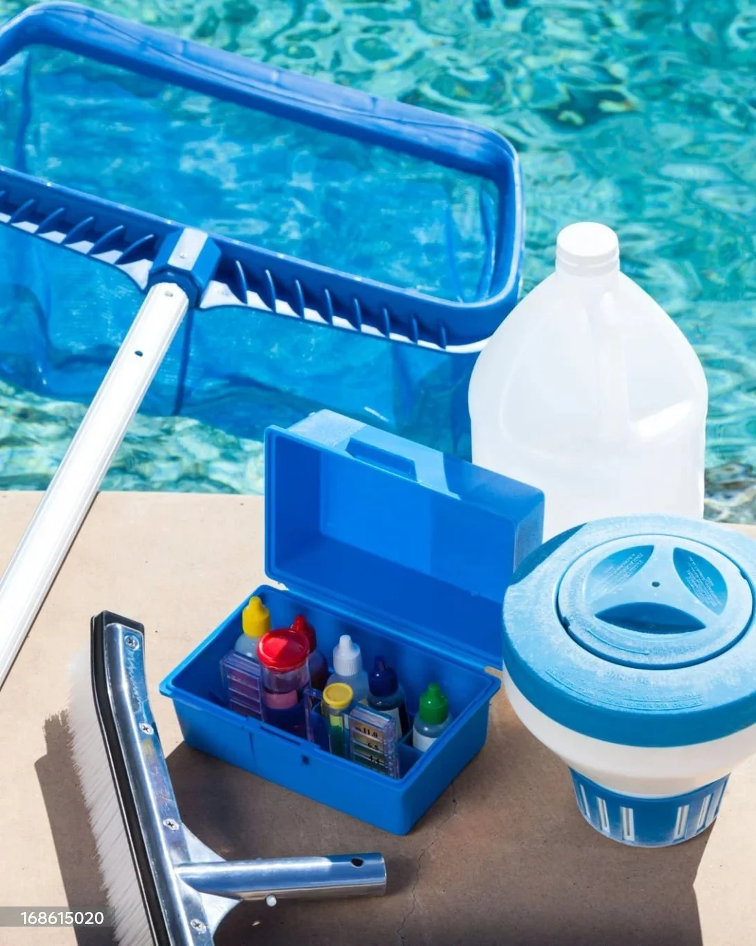 Pool cleaning supplies including a leaf skimmer, bottle of pool chemicals, a small toolbox with bottles and test strips, and a pool filter, placed near the edge of a swimming pool.