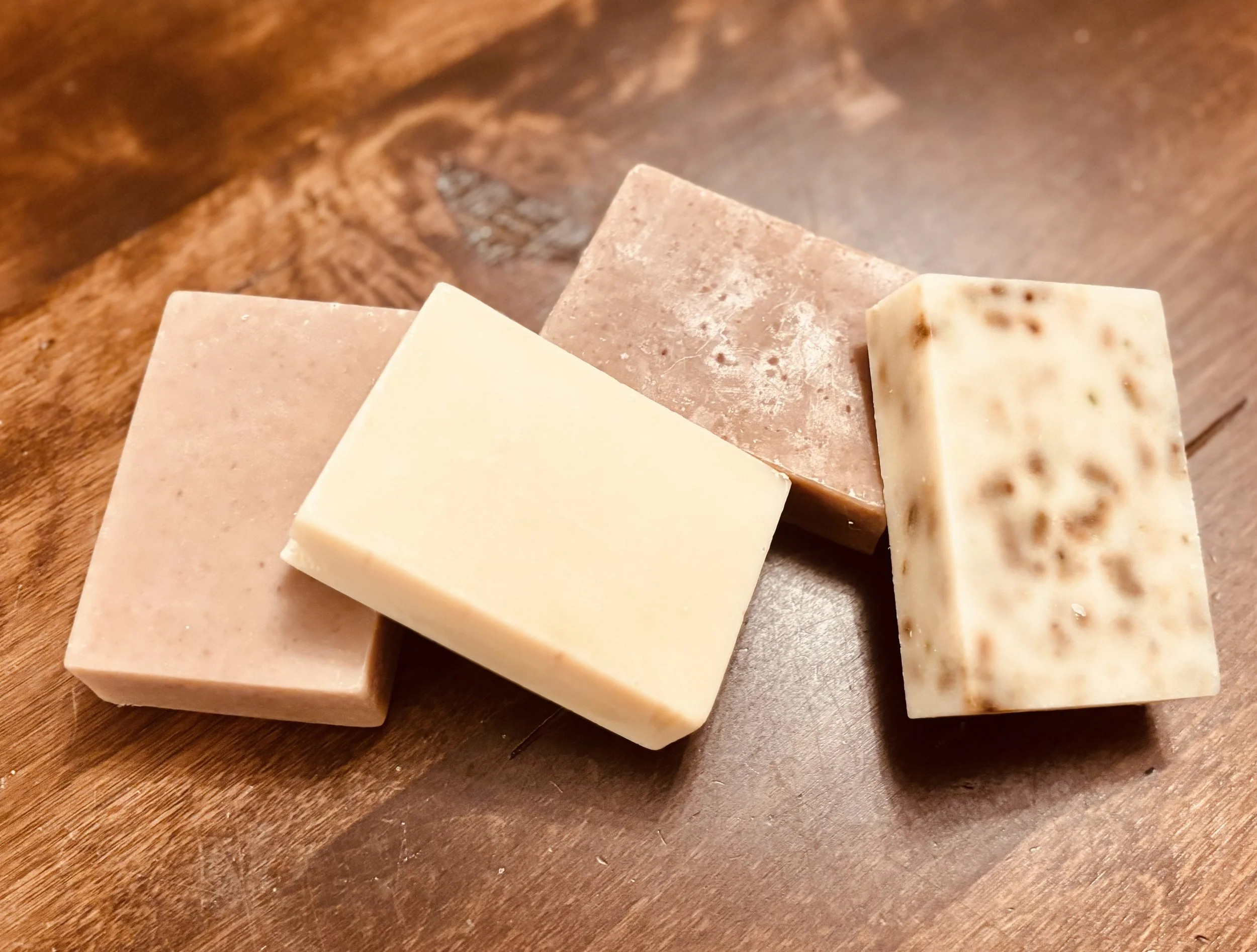 Four different bars of soap on a wooden surface.