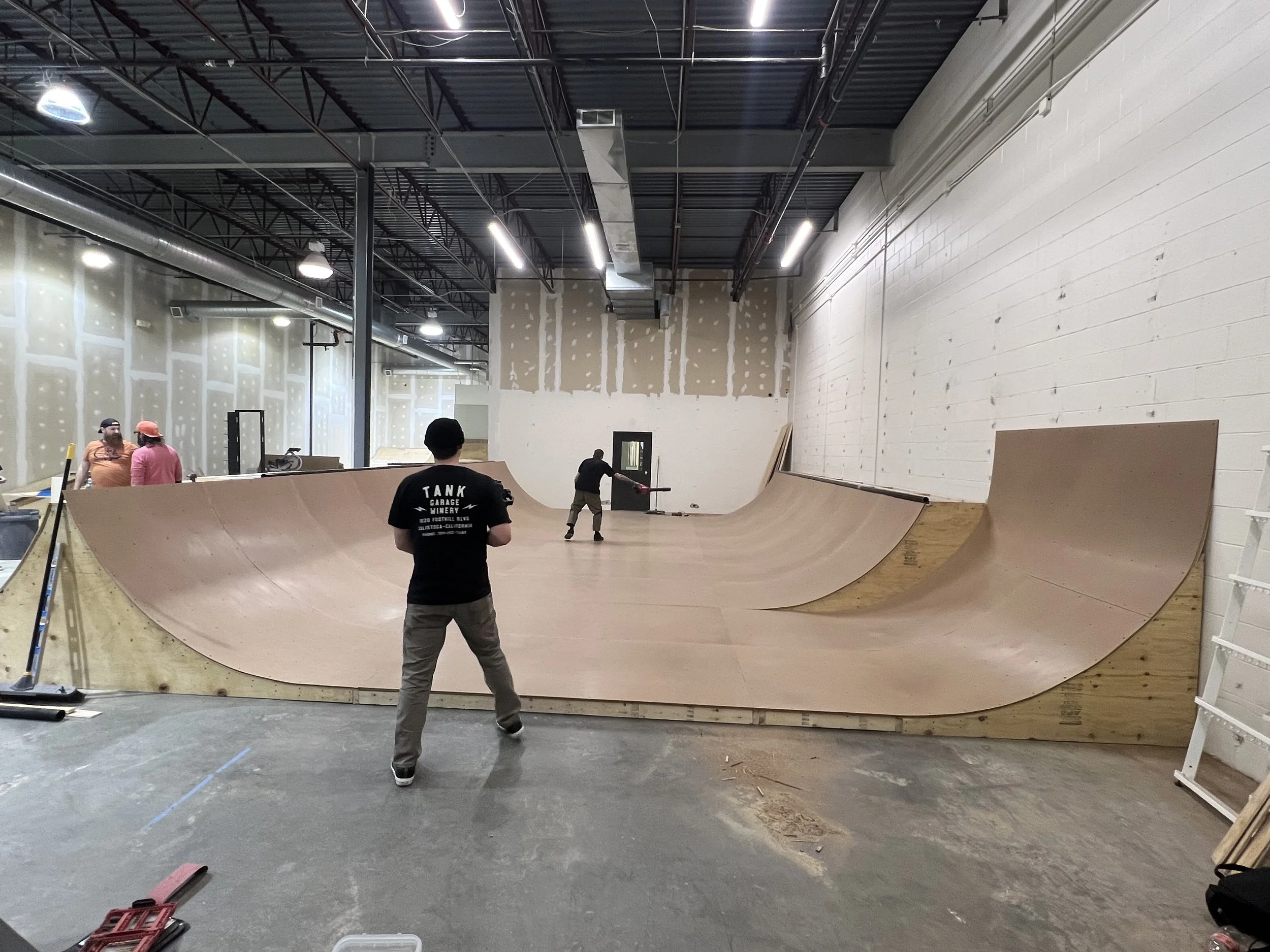 Indoor skate park with wooden ramps and people practicing tricks.