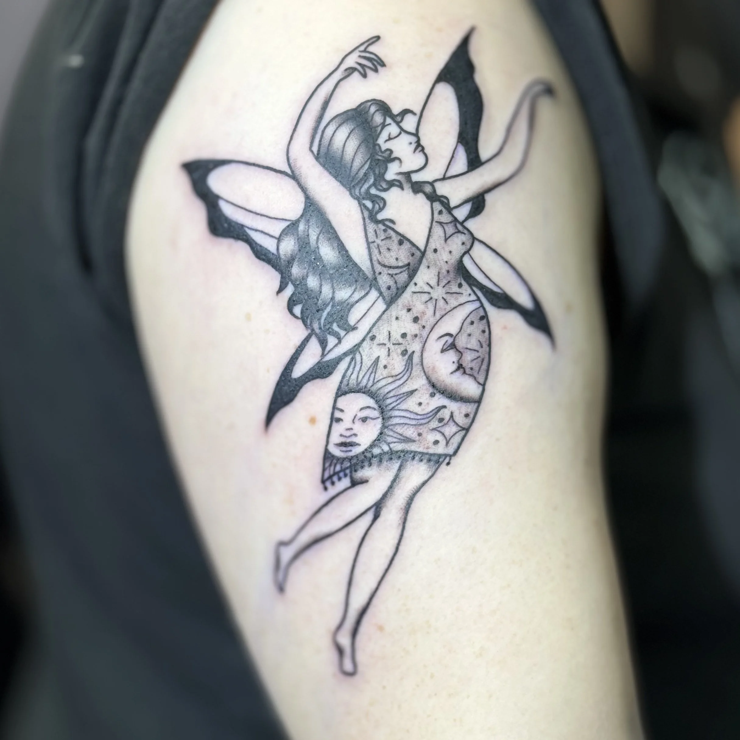 Tattoo of a fairy with butterfly wings, with celestial imagery including the moon, sun, and stars on her body, on a person's arm.