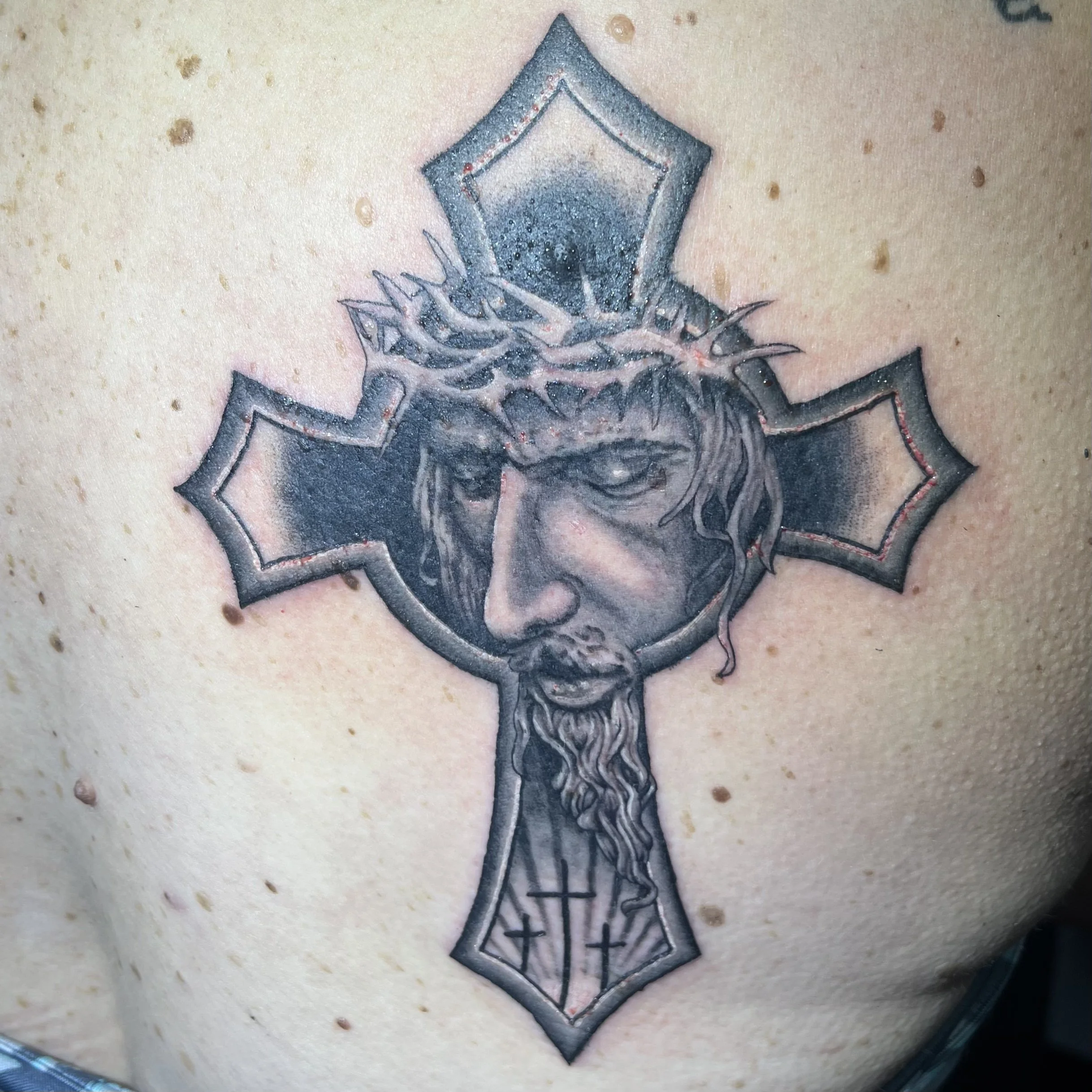 Tattoo of a man with a crown of thorns and a beard, framed by a cross with detailed shading and outlines.