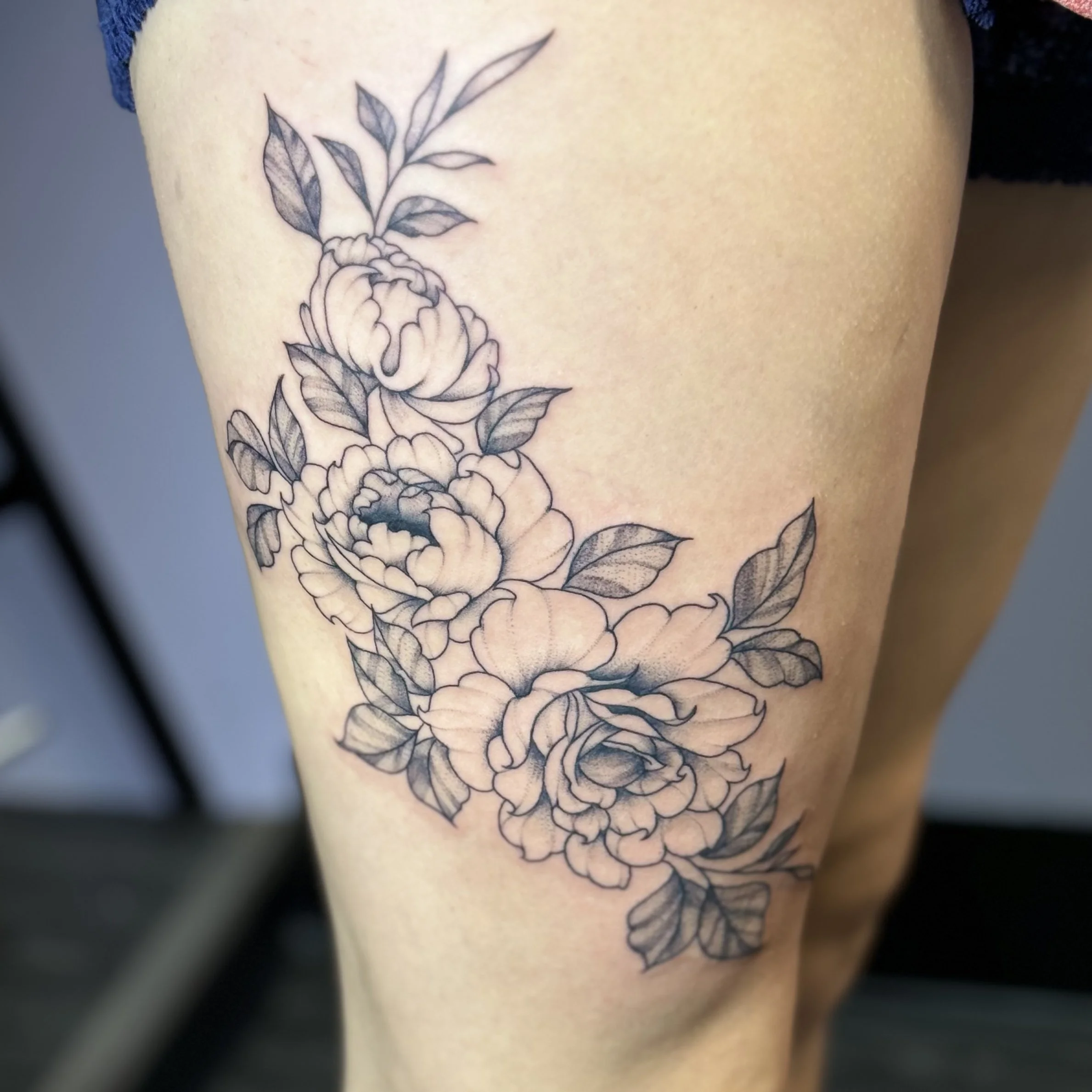 Black and gray floral tattoo featuring peonies and leaves on a person's thigh.