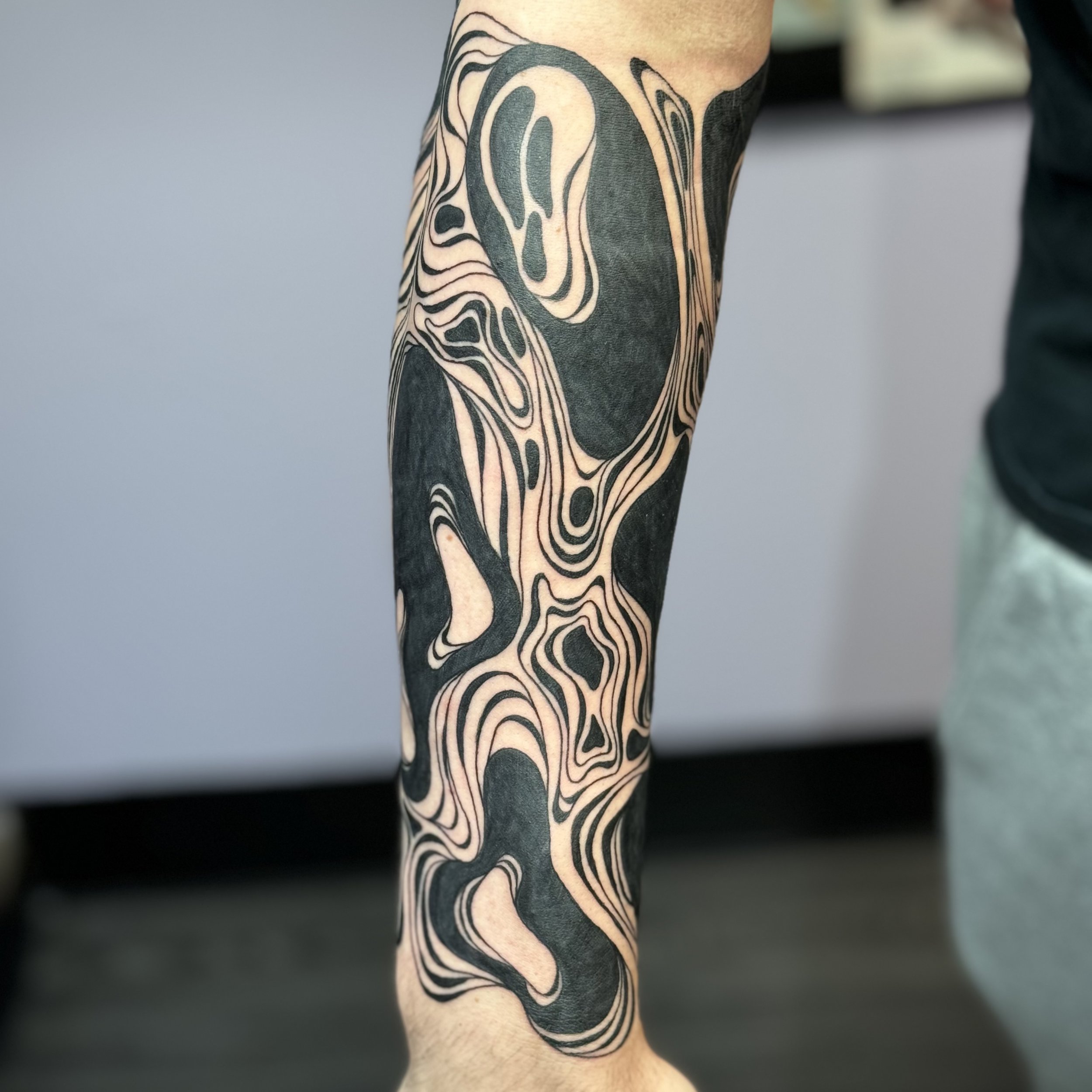 Close-up of a person's arm with a black and beige abstract tattoo design featuring intricate swirling patterns.