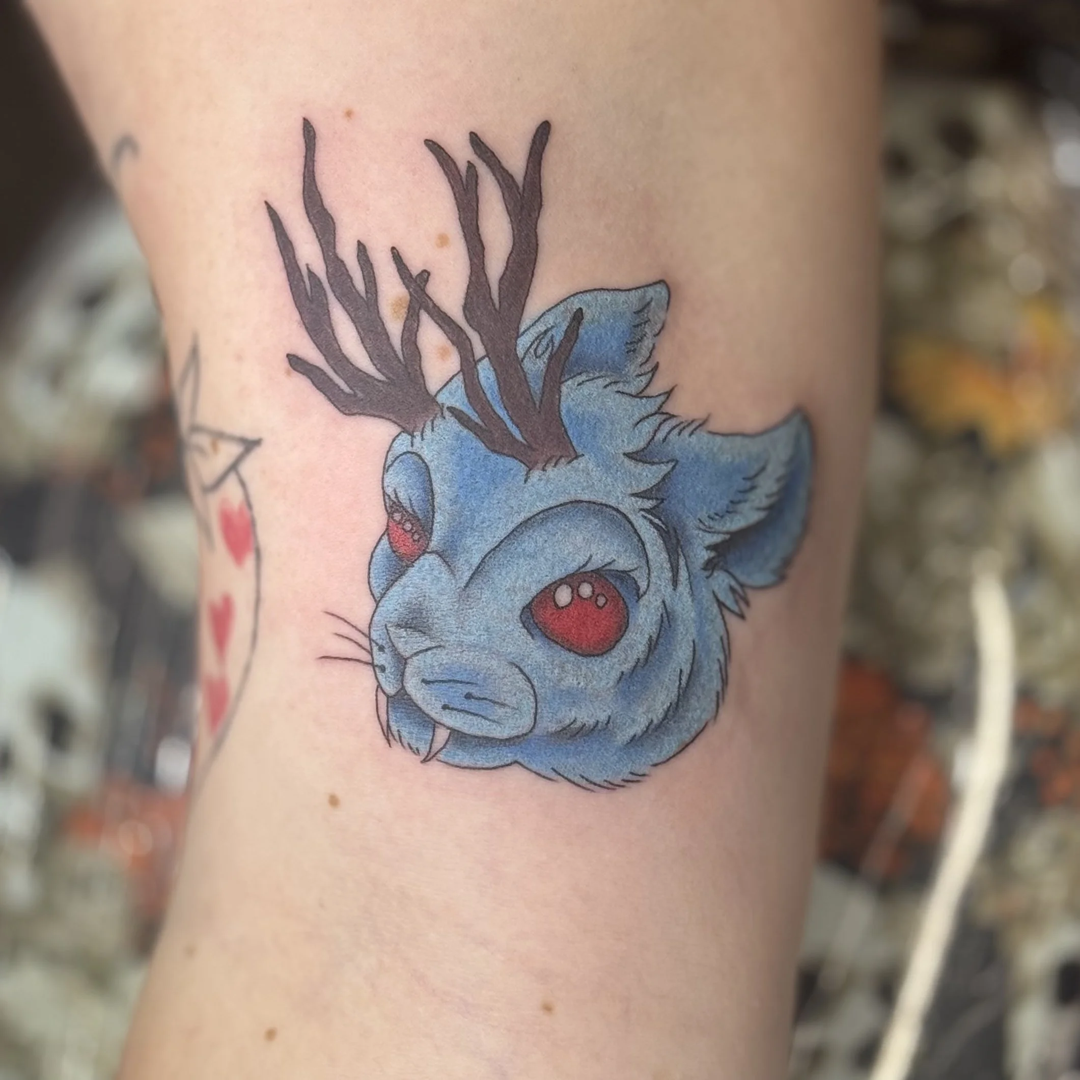 A colorful tattoo of a blue deer with red eyes and dark brown antlers on a person's arm.