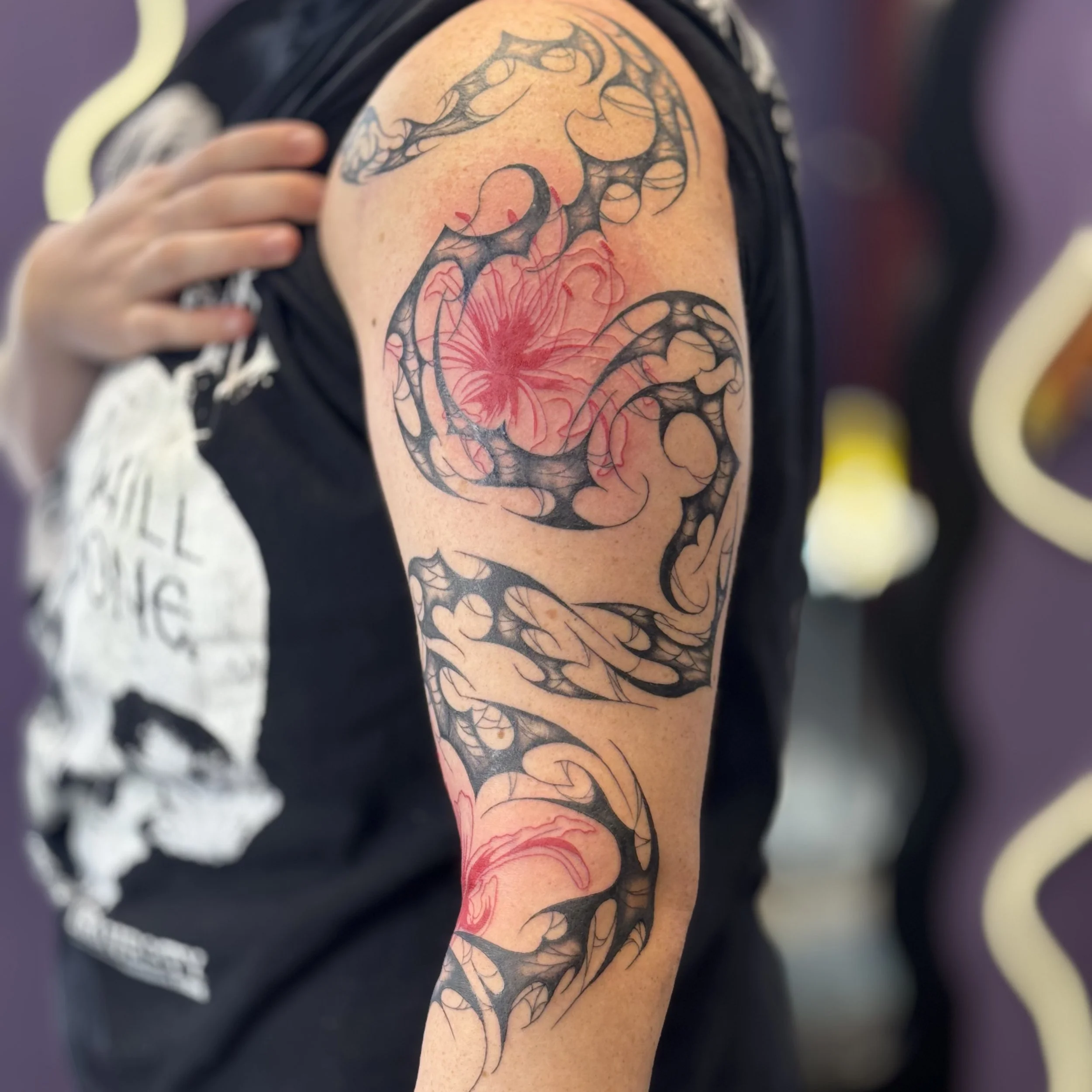 Tattoo of black, swirling, tribal-style patterns with red floral accents on a person's upper arm and shoulder.