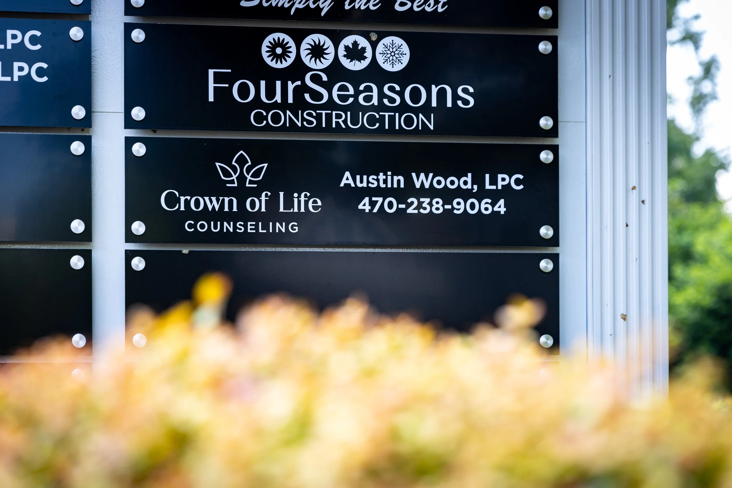 Signboard with company names and contact information at a construction site. FourSeasons Construction and Crown of Life Counseling, with contact details for Austin Wood, LLC.