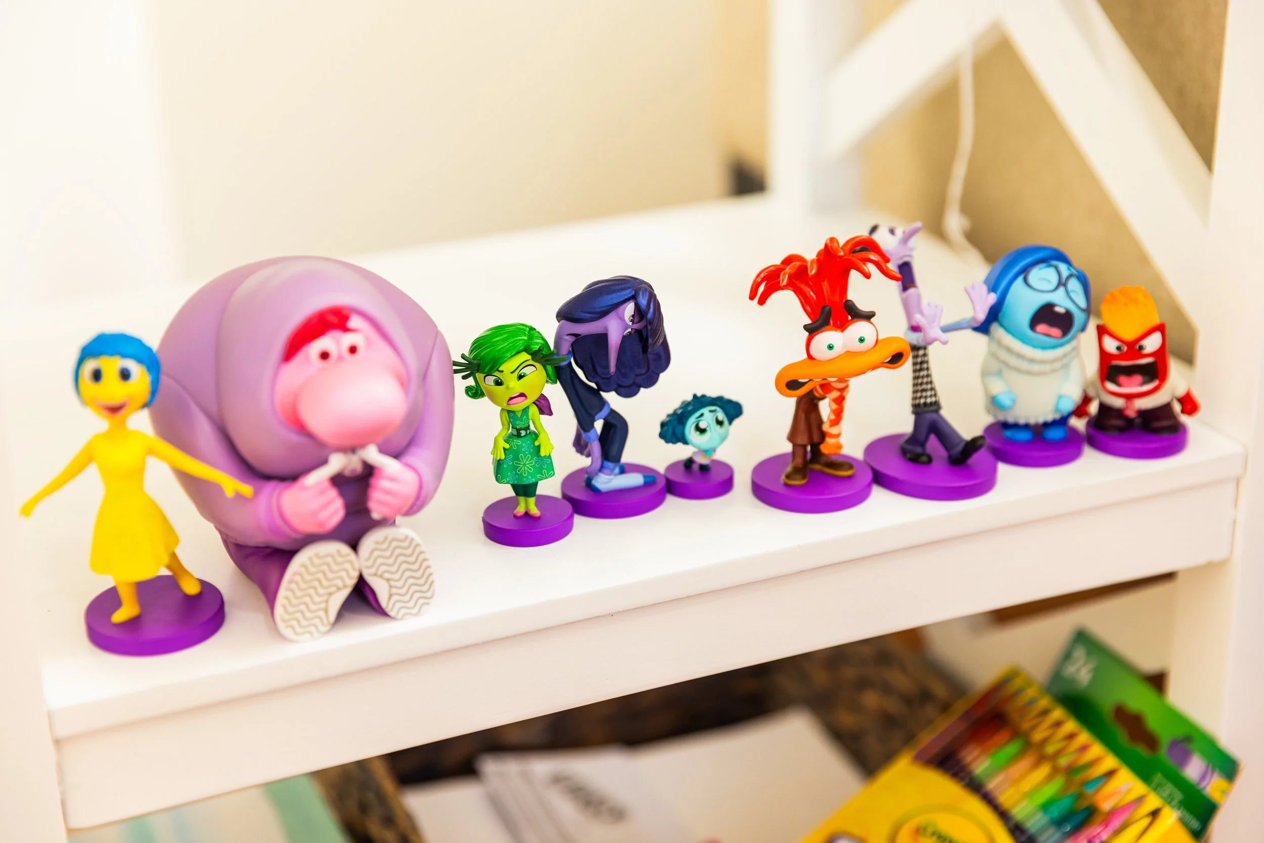 Collection of colorful small figurines from the movie Inside Out on a white shelf.