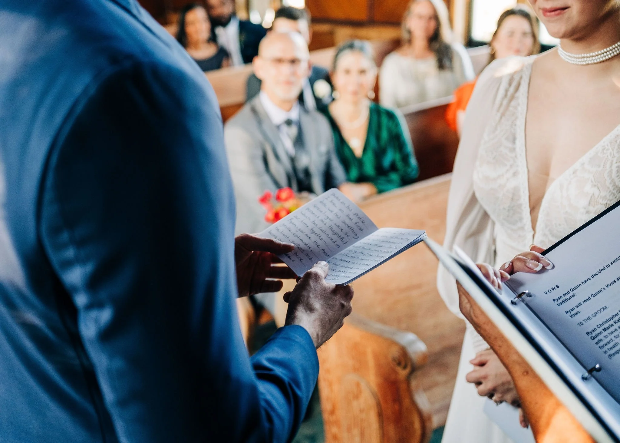 A wedding ceremony with the bride and groom exchanging vows, reading from papers, with guests seated in the background.