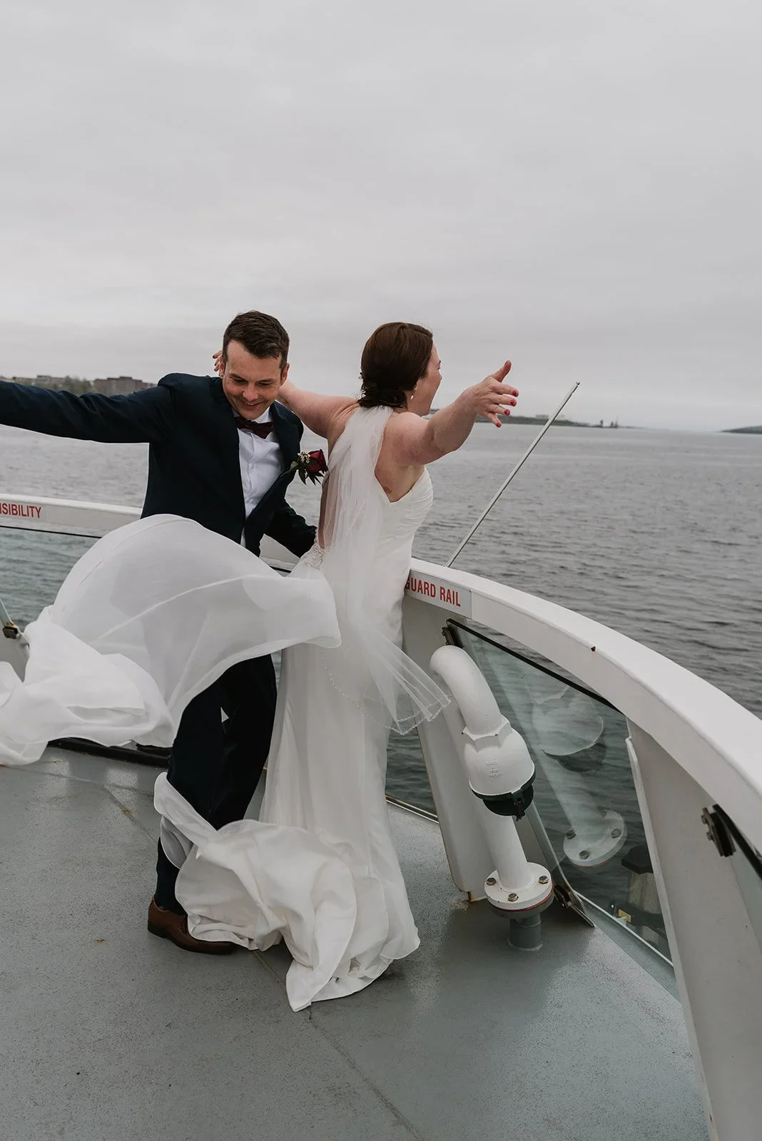 Bride and groom dancing on a boat with the water and overcast sky in the background.