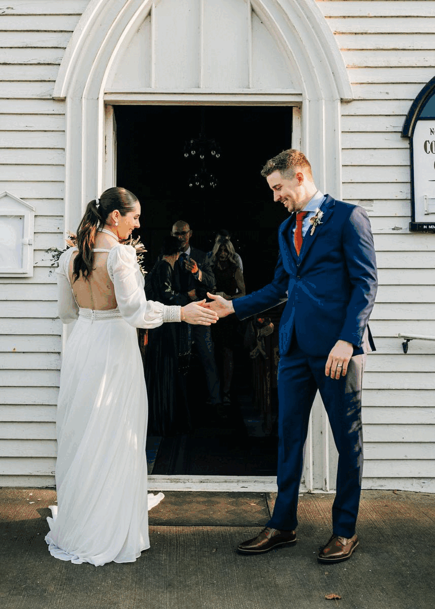 A bride and groom holding hands outside a church doorway during their wedding ceremony.