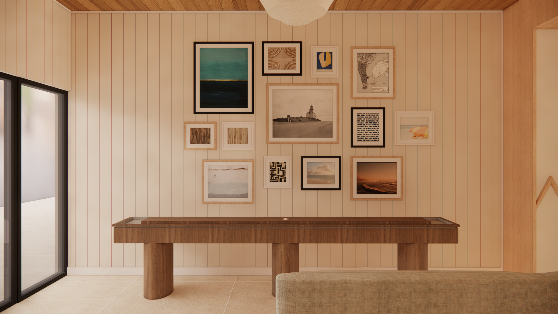 A living room with a wall decorated with various framed pictures and artwork, a wooden console table, a sliding glass door on the left, and a beige sofa in the foreground.