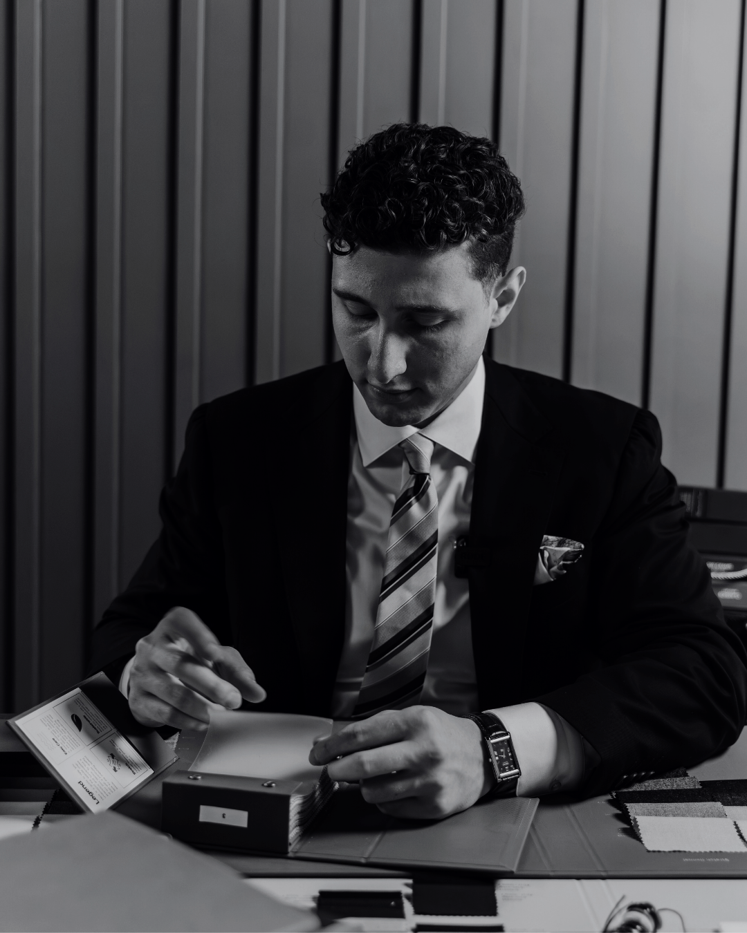 A man in a suit and tie sitting at a table, examining color swatches and a brochure.