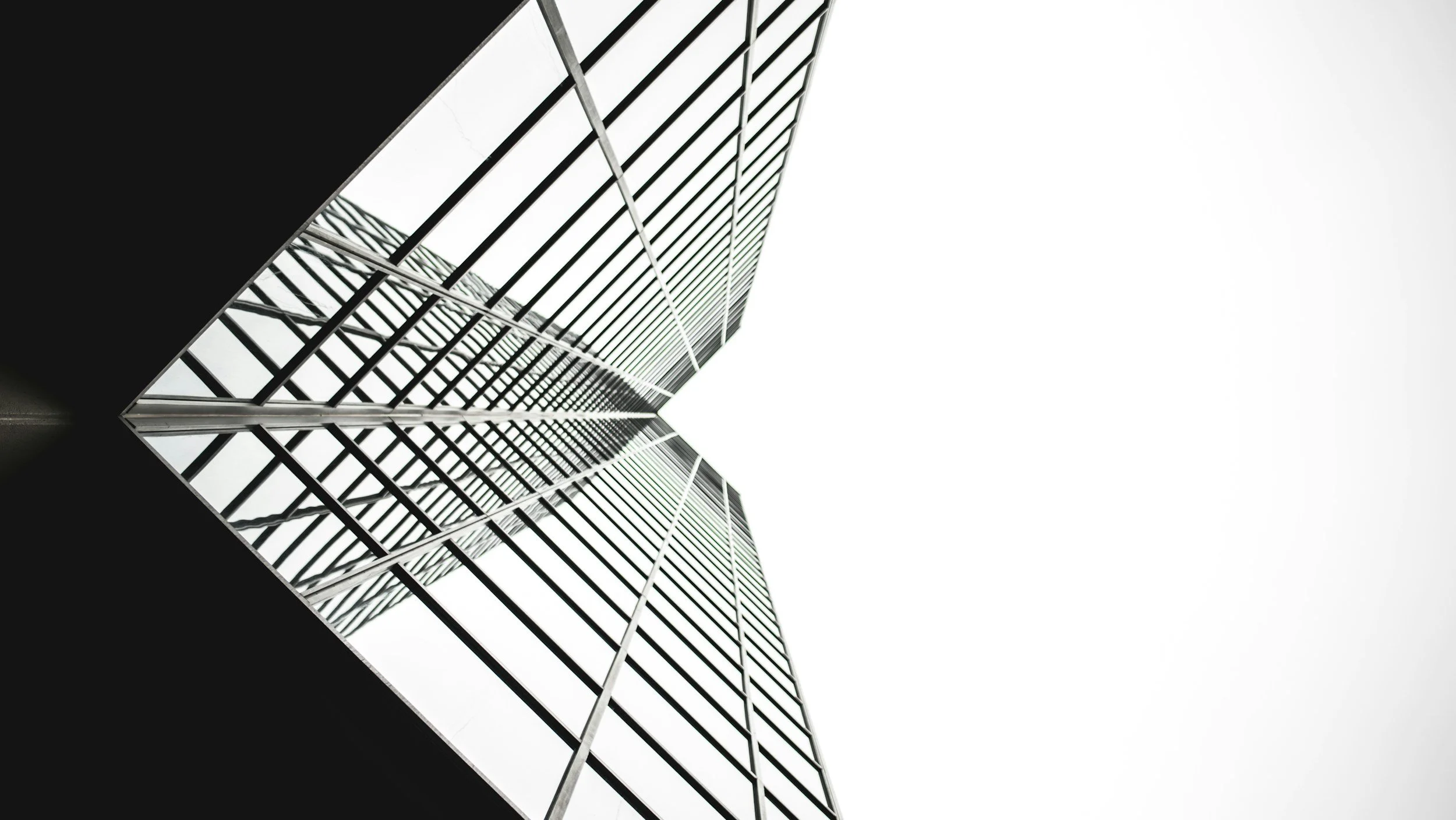 Looking up at a modern skyscraper with a mirrored glass facade in black and white, emphasizing geometric lines and reflective surfaces.