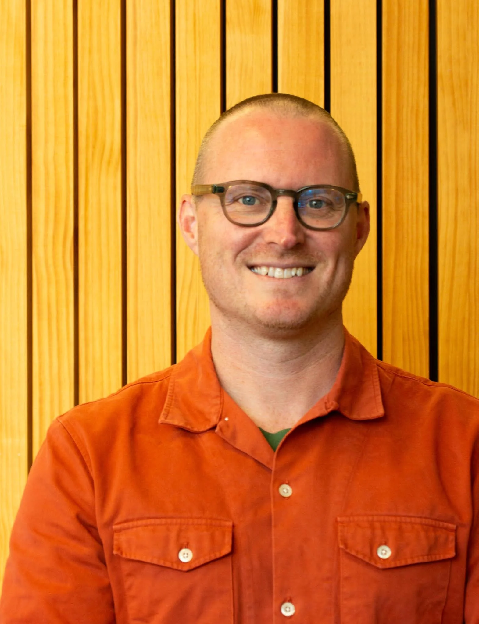 Photo of Joe Slater from Cascade Coaching, smiling, wearing an orange shirt, standing in front of a wooden wall.